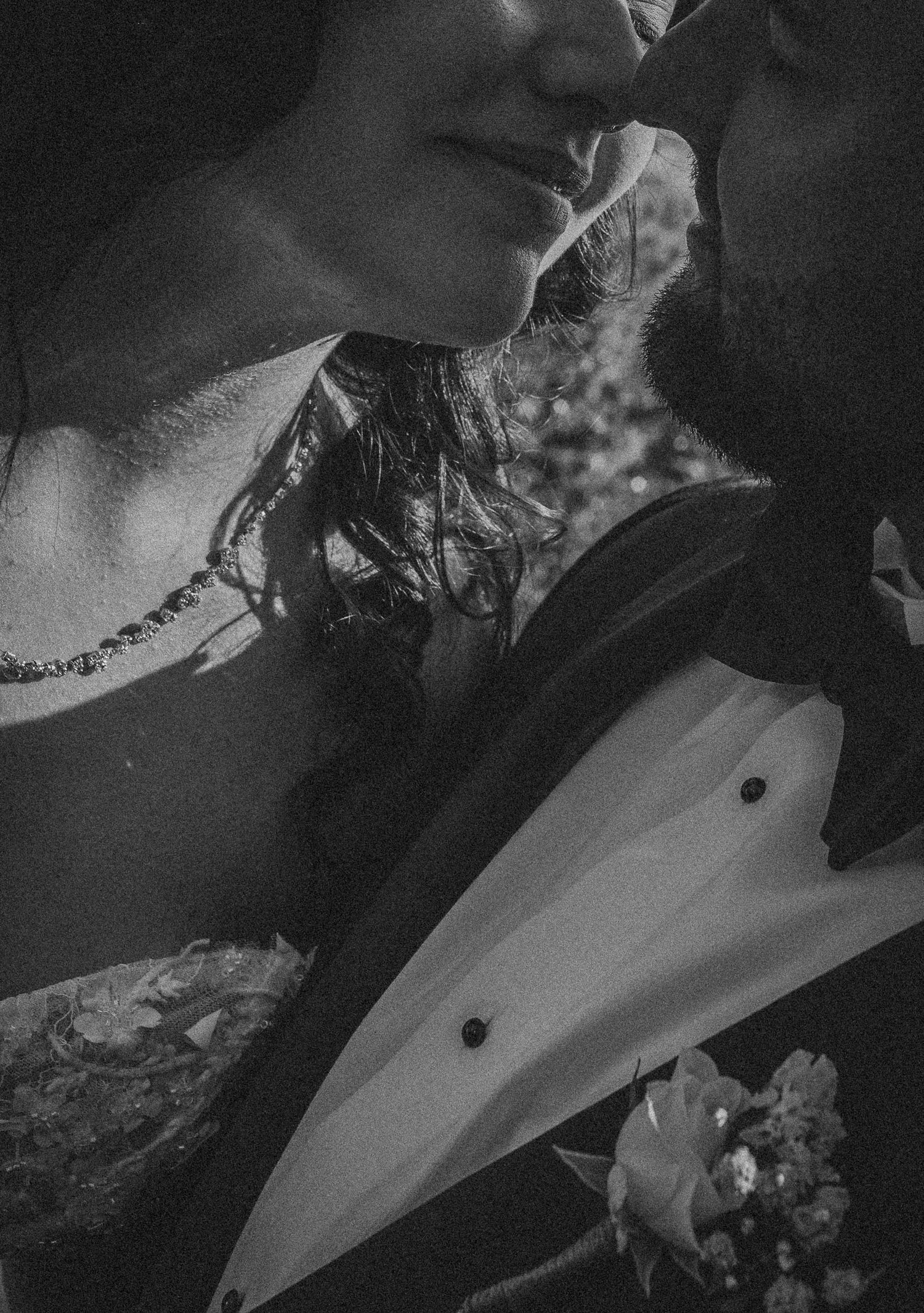 Black and white close-up of a bride and groom sharing a romantic moment, bride wearing a necklace and strapless gown.