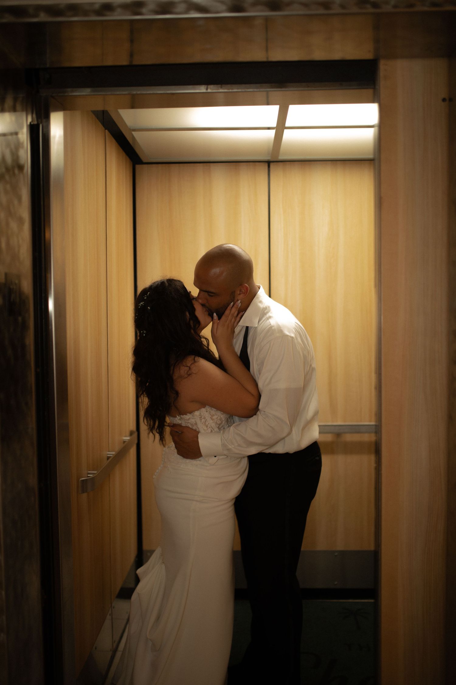 Bride and groom sharing a romantic kiss inside an elevator on their wedding day.