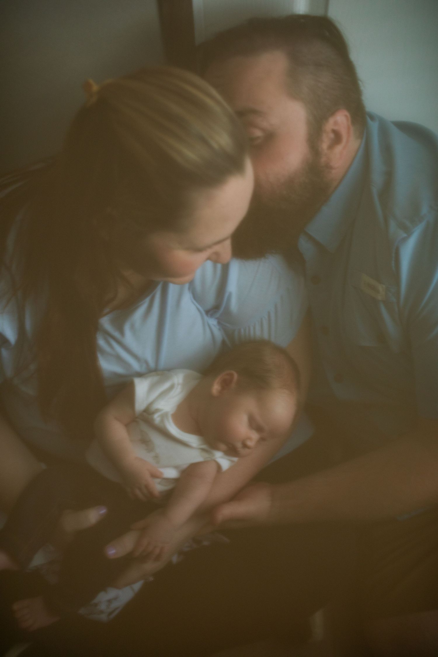 New parents tenderly gaze at their sleeping newborn baby in a soft, warmly lit intimate family portrait.