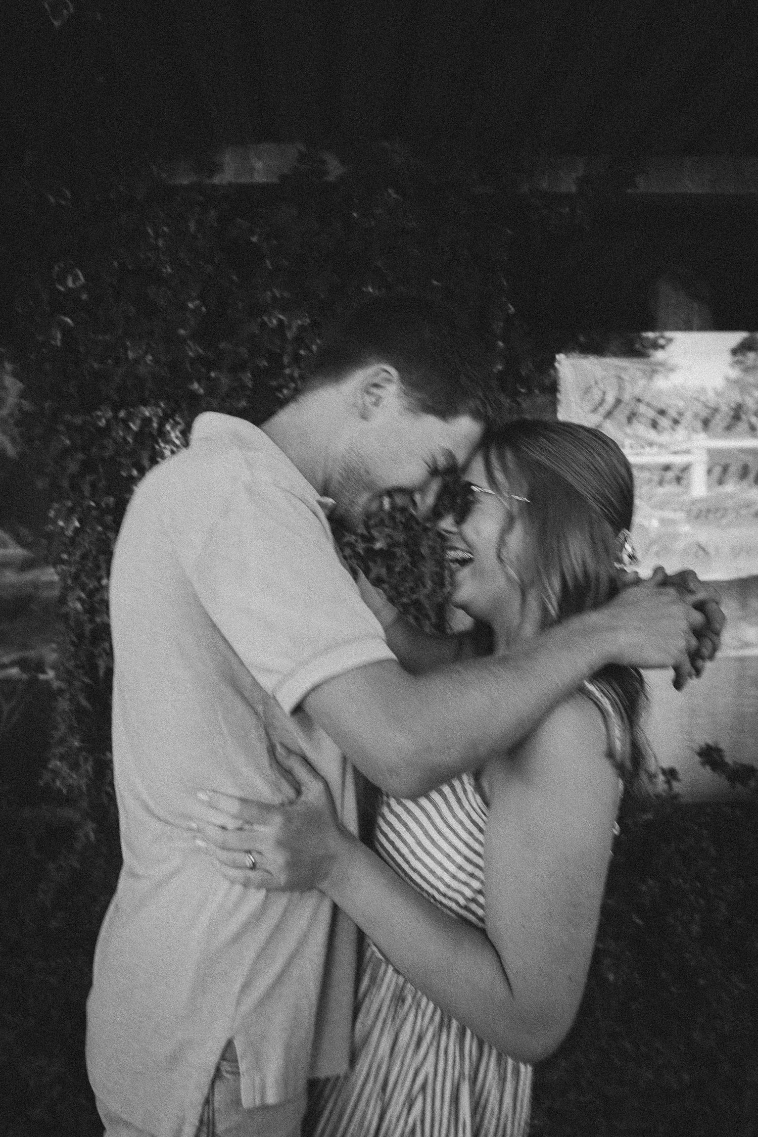 A romantic black and white portrait of a couple embracing outdoors in an intimate tender moment.