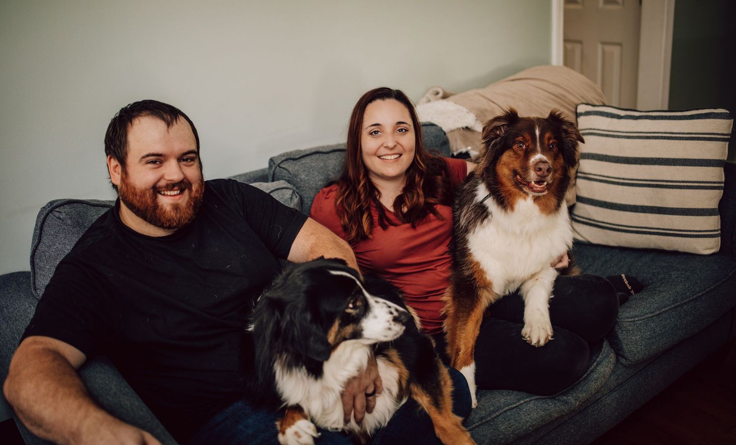 Relaxed family moment on couch with two dogs in natural indoor lighting.