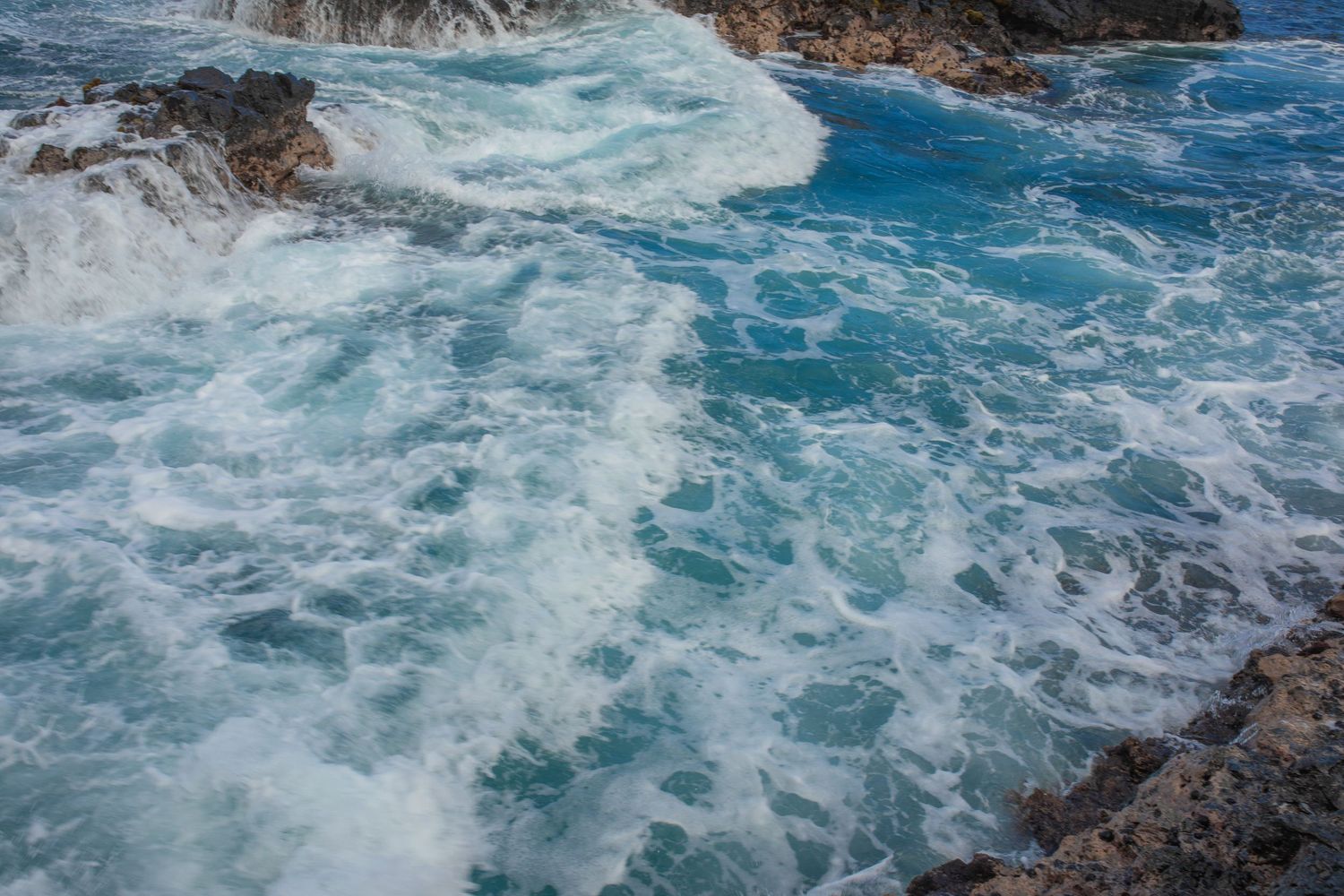 Turbulent blue ocean waves crashing against rocky coastal cliffs with white foamy spray in dramatic motion.