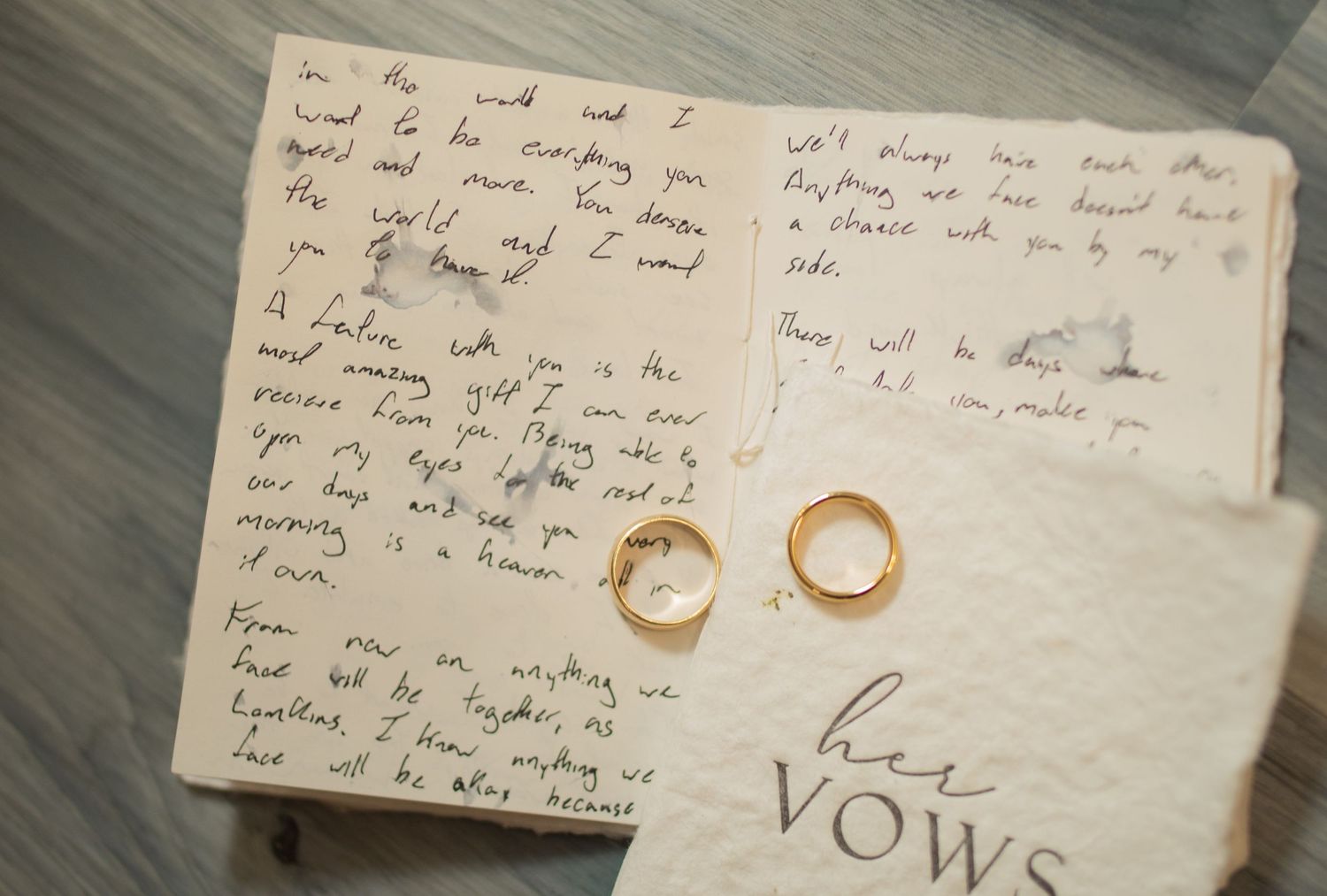 Two gold wedding bands resting on handwritten wedding vows paper with her vows text visible below.