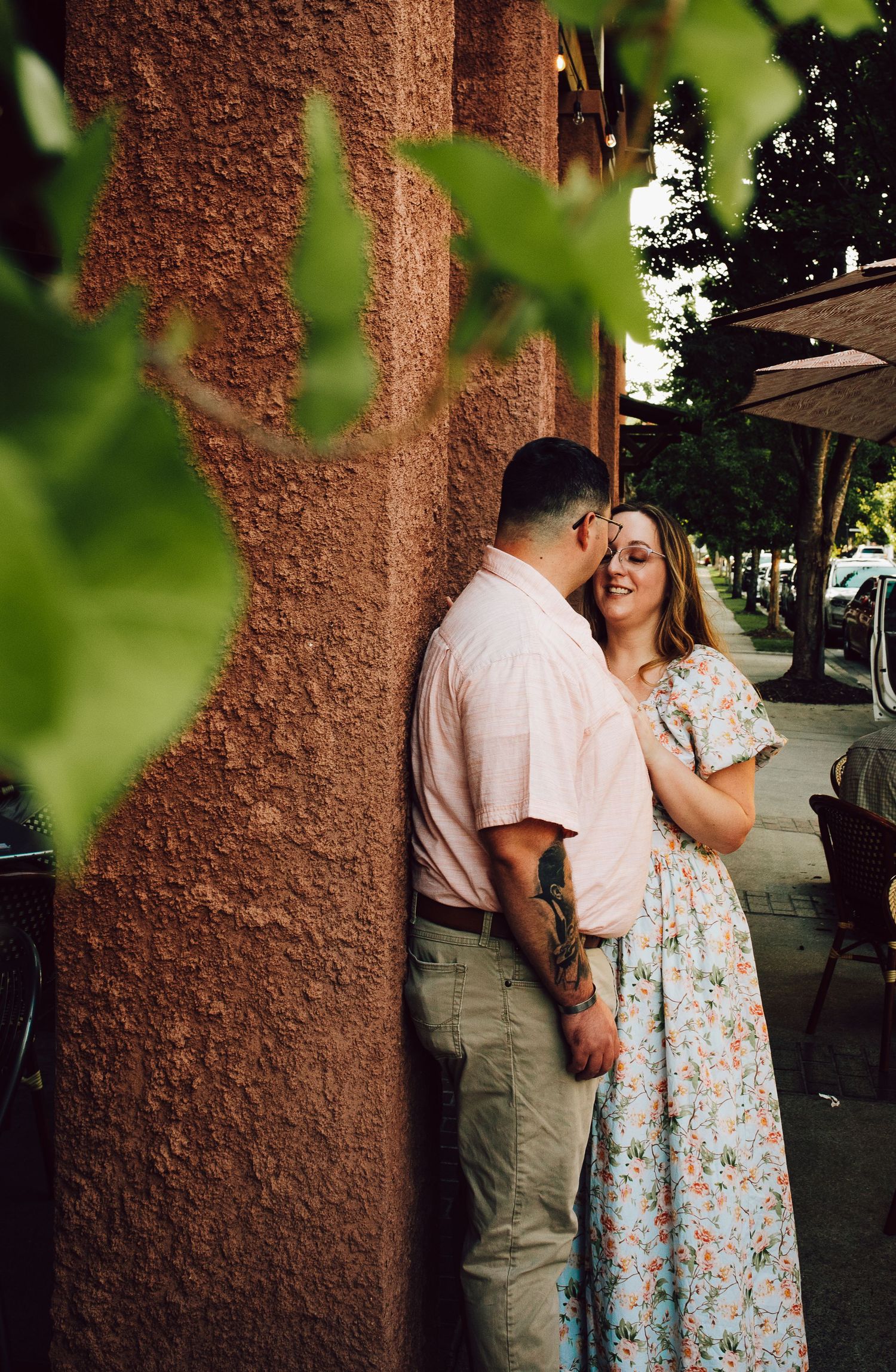 A couple sharing a moment against a textured wall with green foliage in foreground.