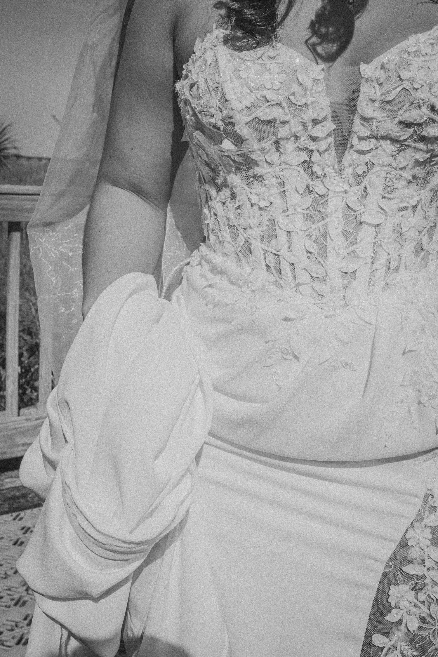 Black and white close-up of a bride in a detailed floral applique wedding gown holding her dress skirt.