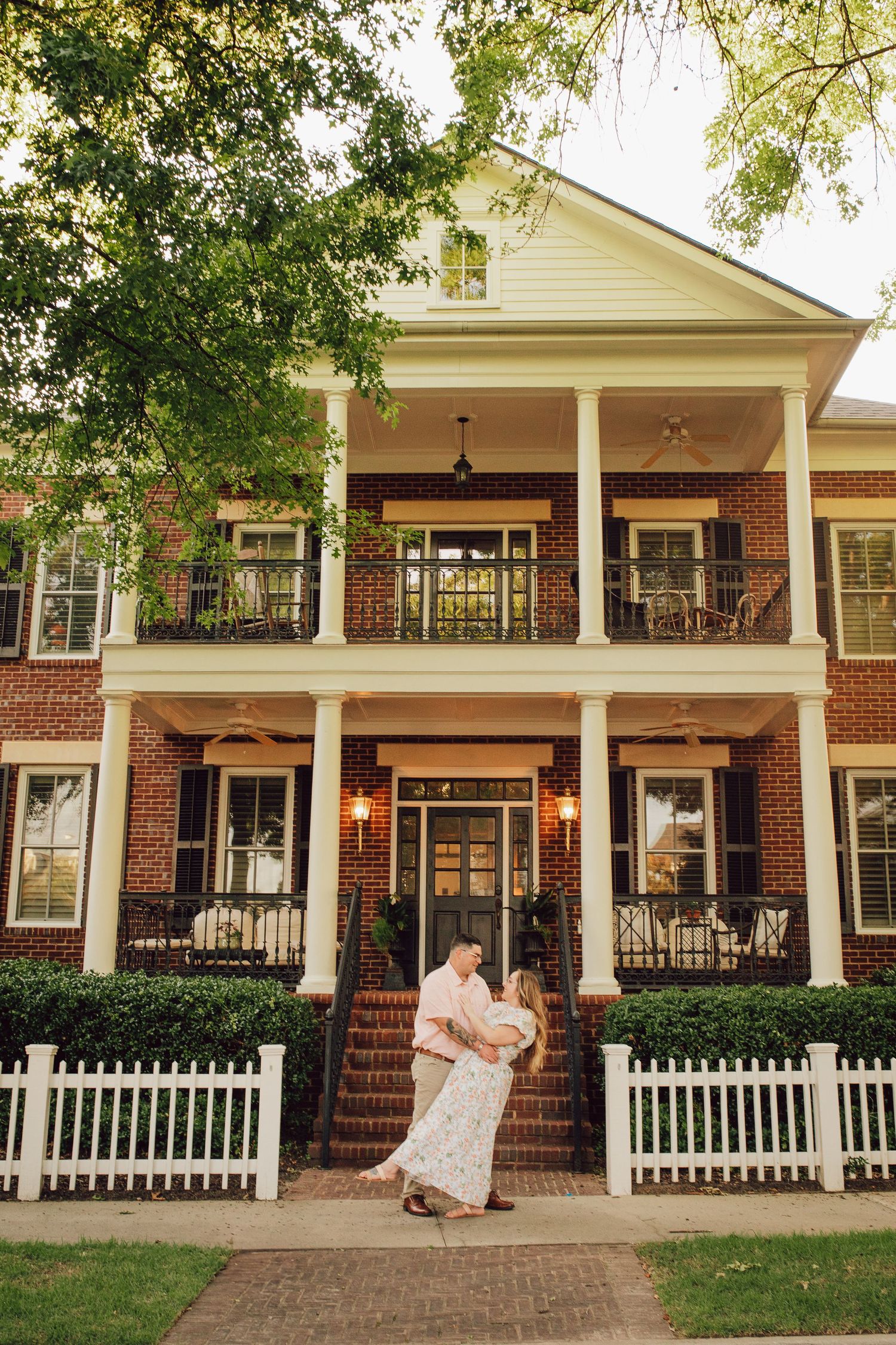 A romantic pose in front of a grand southern colonial style brick house with white pillars.