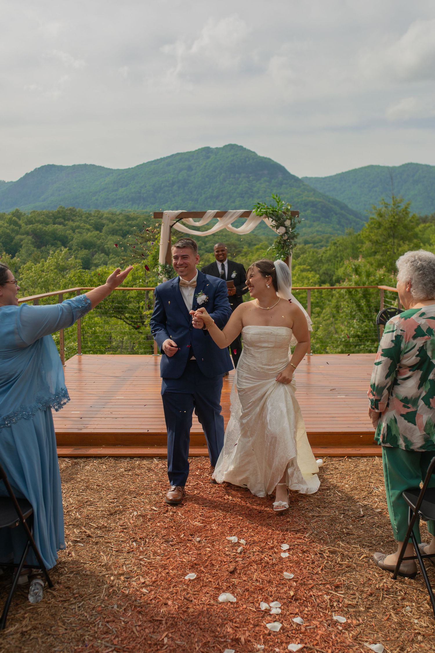 Bride and groom walk down the aisle at an outdoor mountain wedding ceremony with lush green hills backdrop.