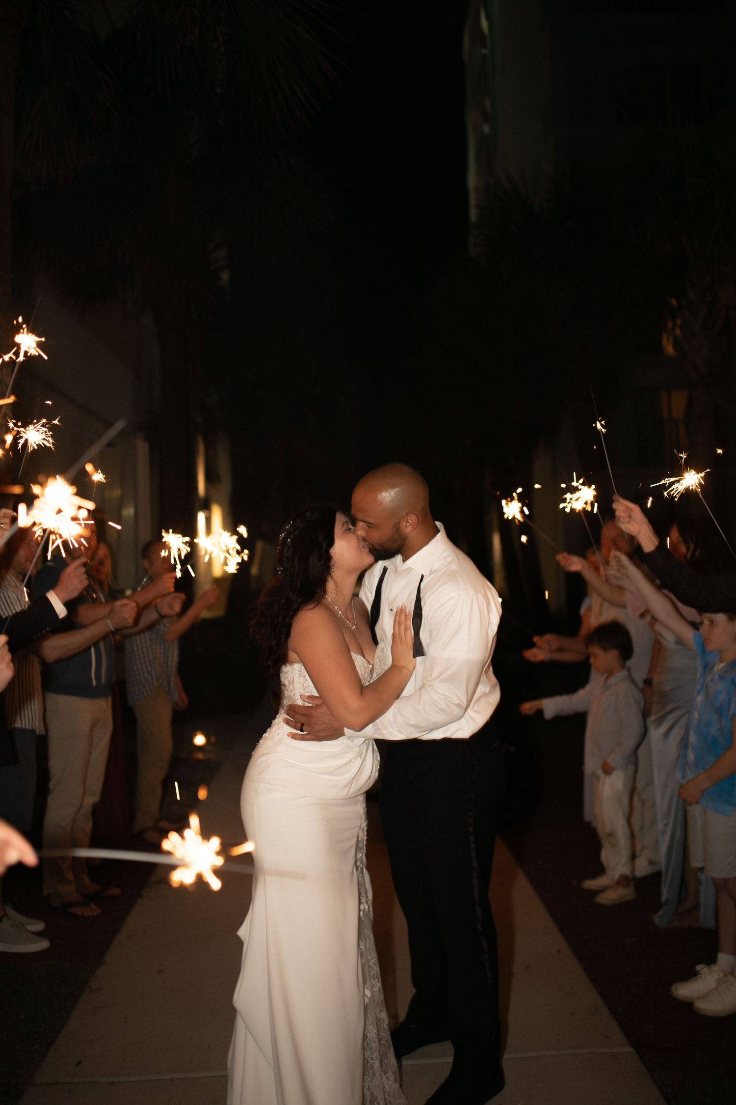 Newlywed couple sharing a romantic kiss during a sparkler exit at their wedding reception at night.