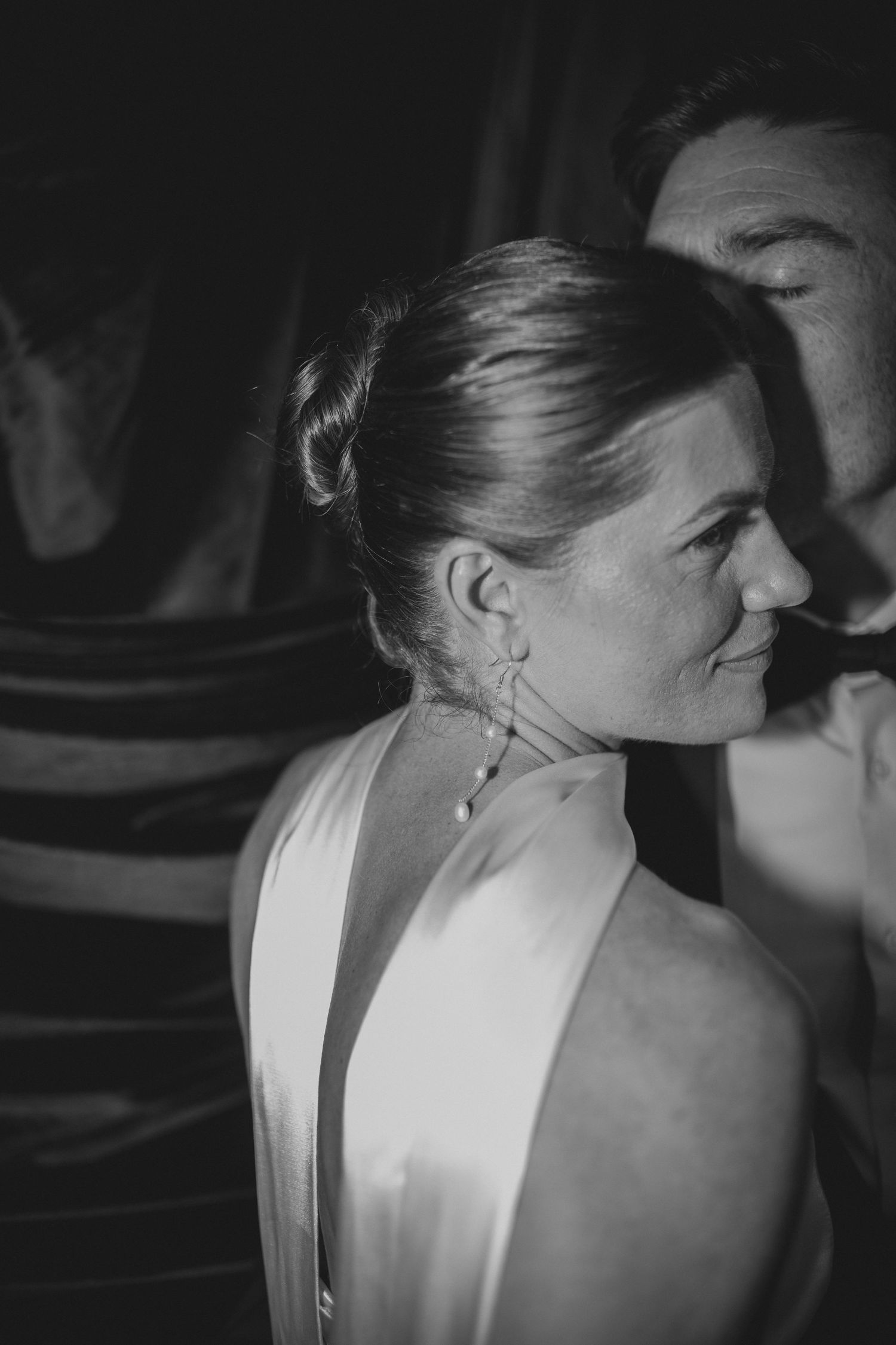 Black and white photo of an elegant woman in a backless dress with an updo hairstyle and dangling earrings at a formal event.