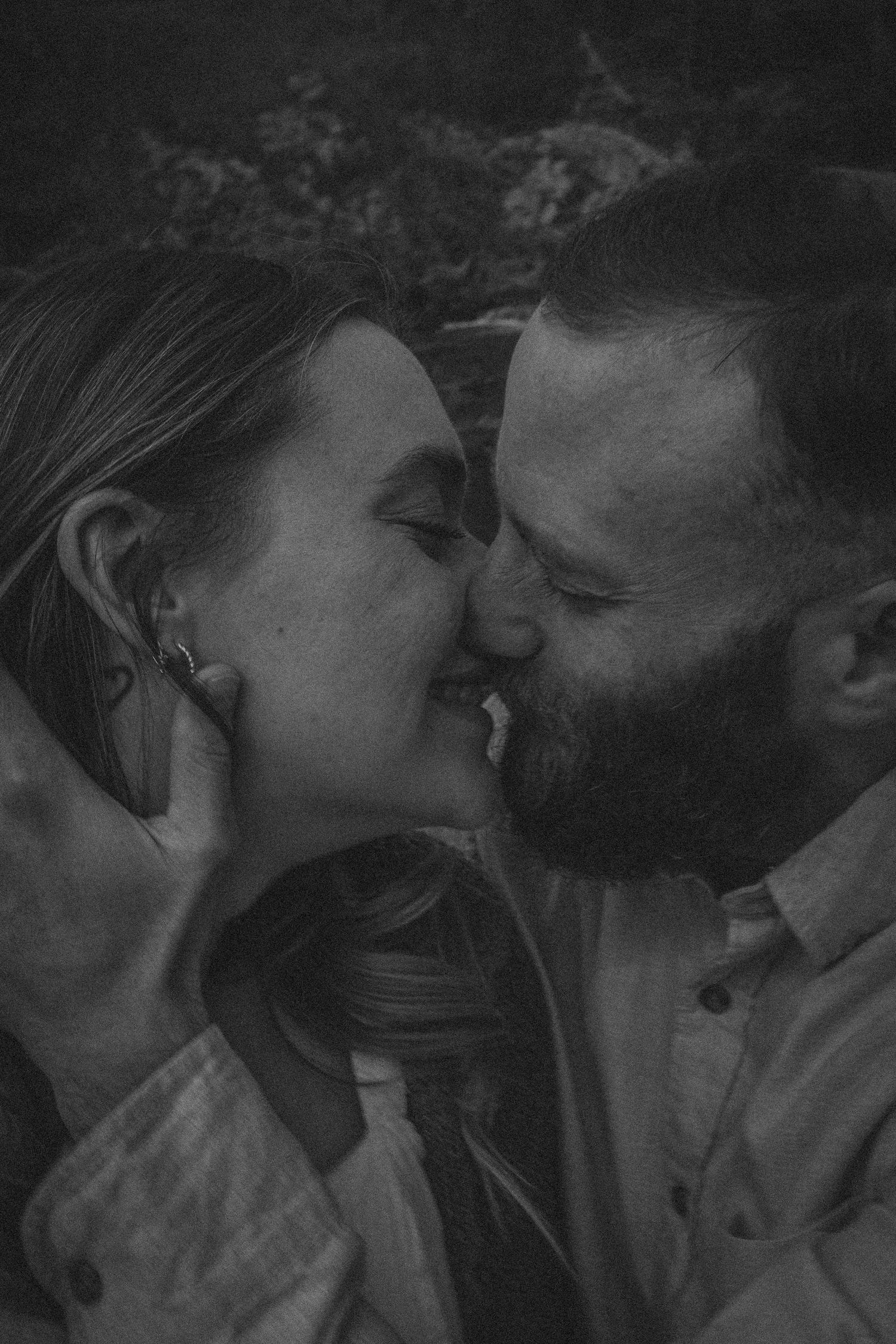 Black and white photo of a couple sharing a tender kiss, faces close together, smiling romantically.