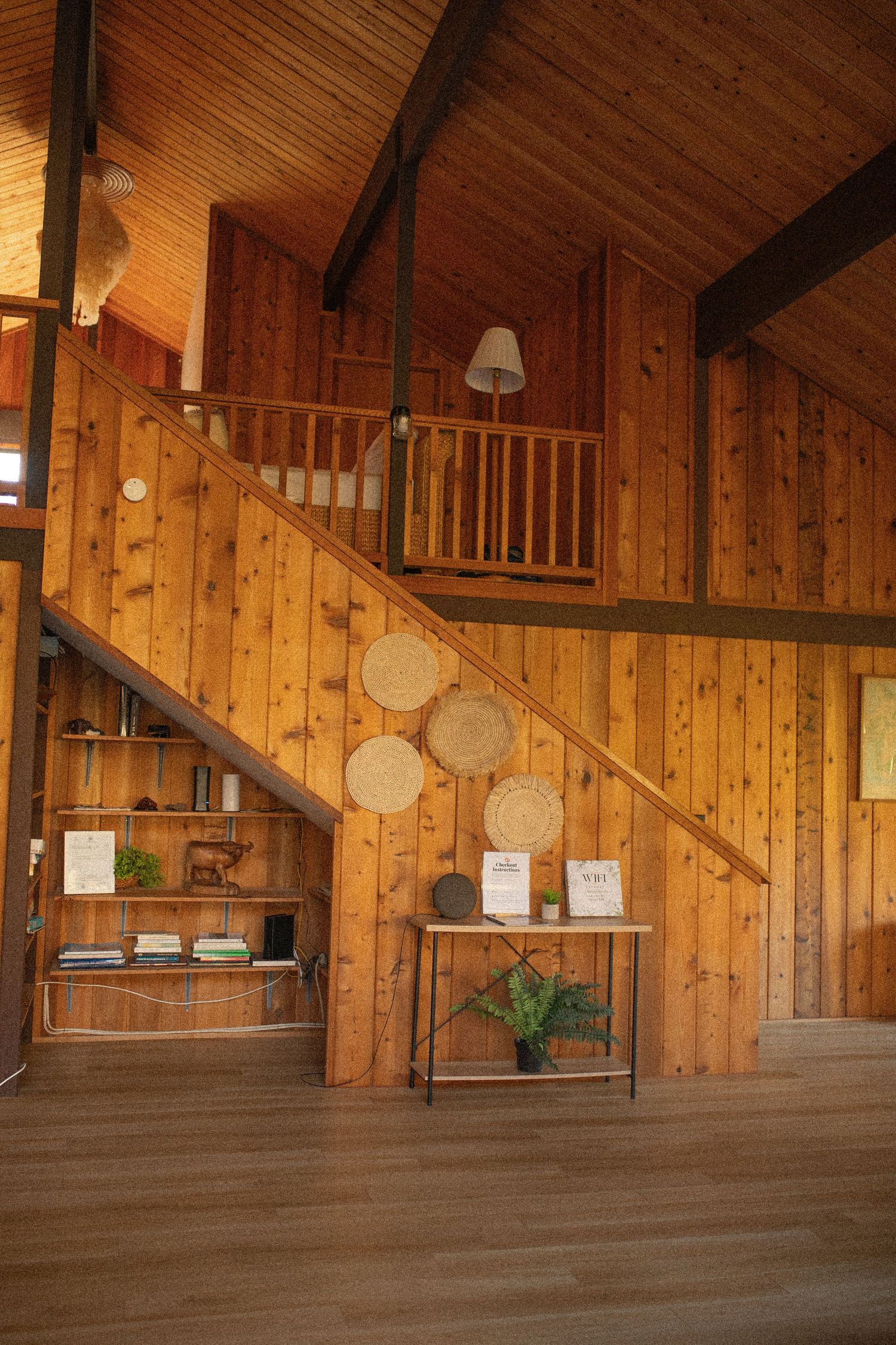 Interior view of a rustic wooden cabin with pine walls, stairs leading to a loft, and decorative wall accents.