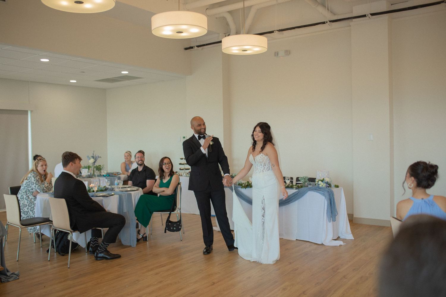 Bride and groom sharing a microphone during wedding reception speech in bright modern venue with seated guests.
