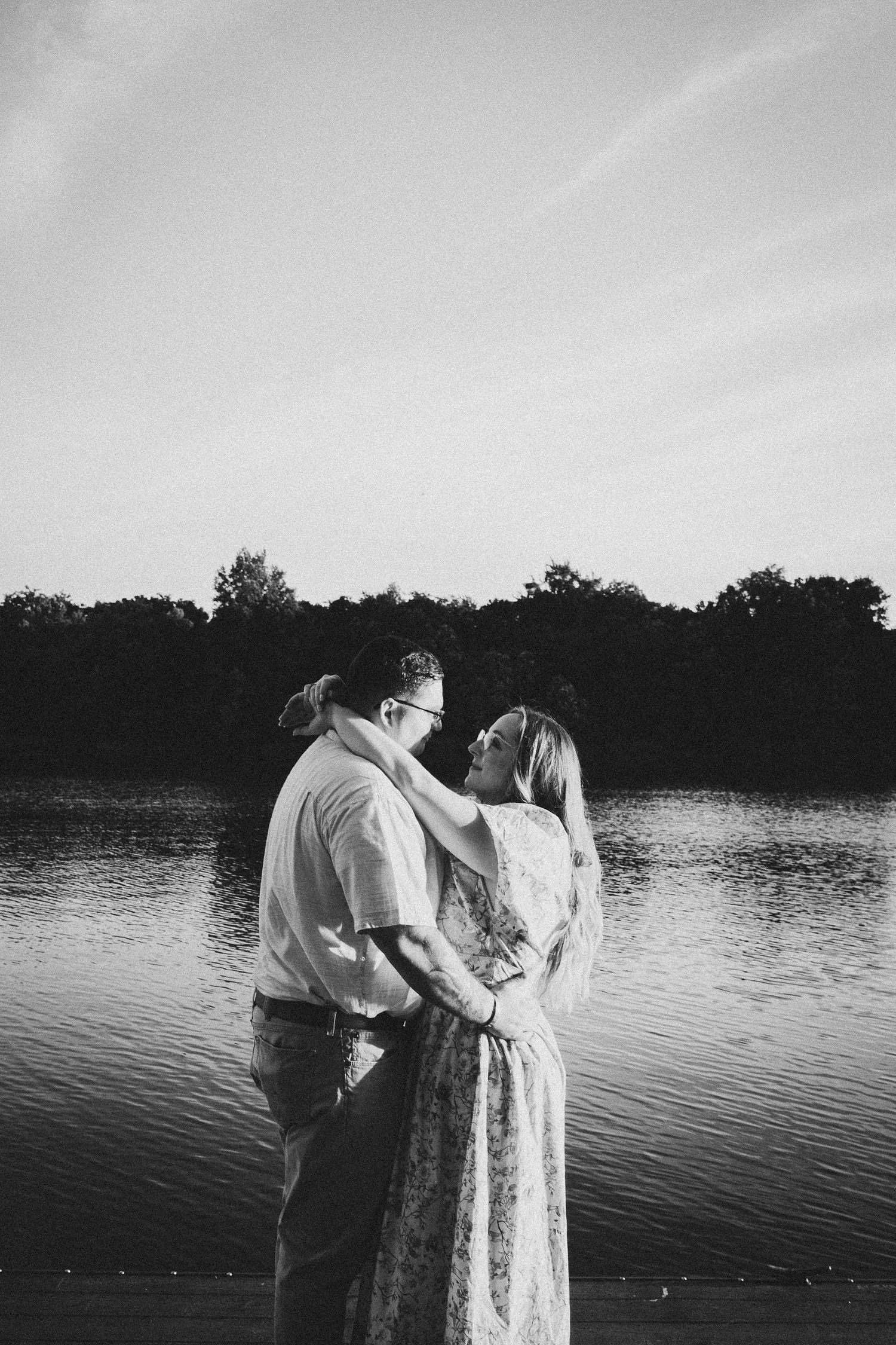 A romantic black and white silhouette of a couple by a serene lake at dusk.