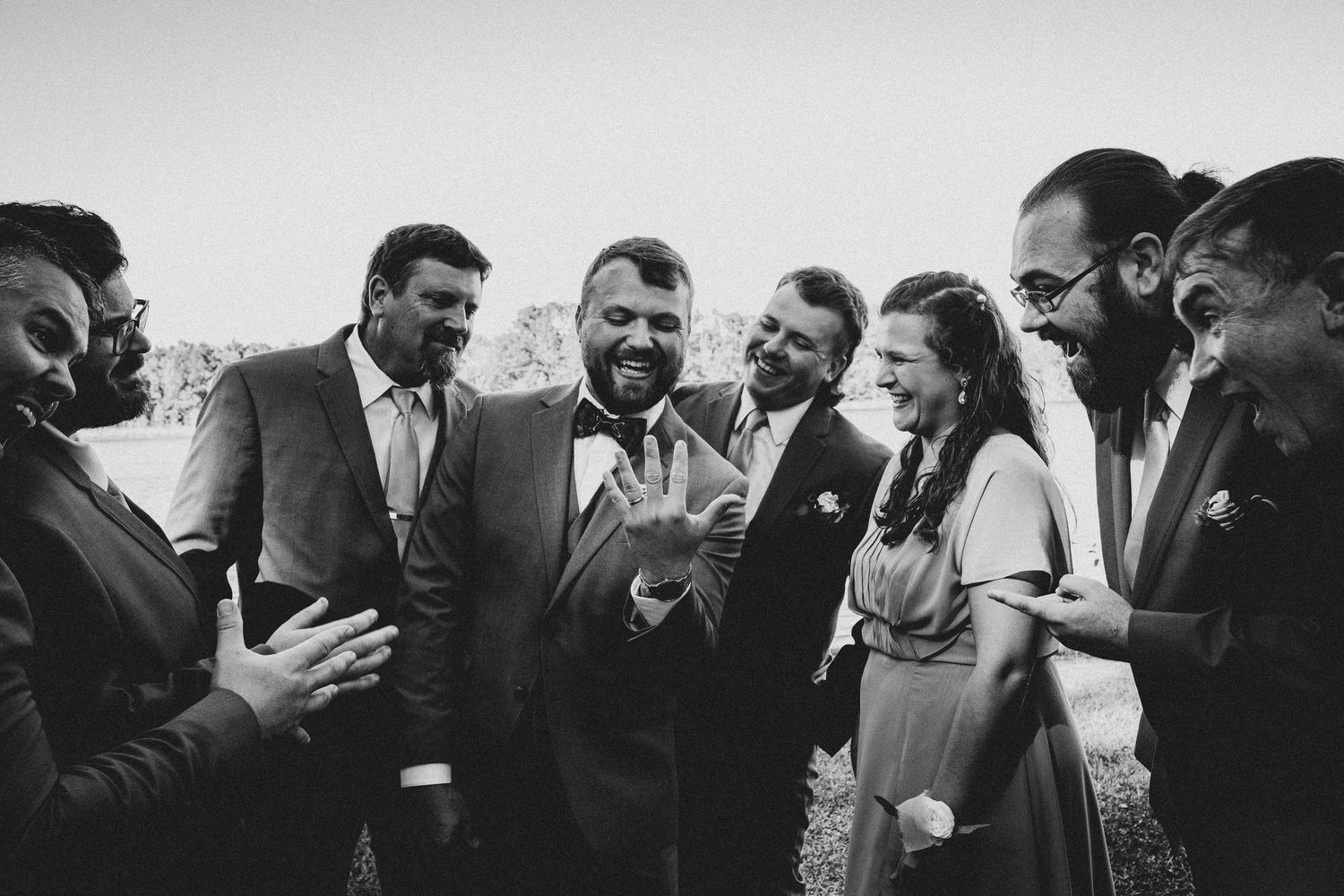 A candid black and white photo of a joyful group in formal attire laughing and sharing a moment together outdoors.