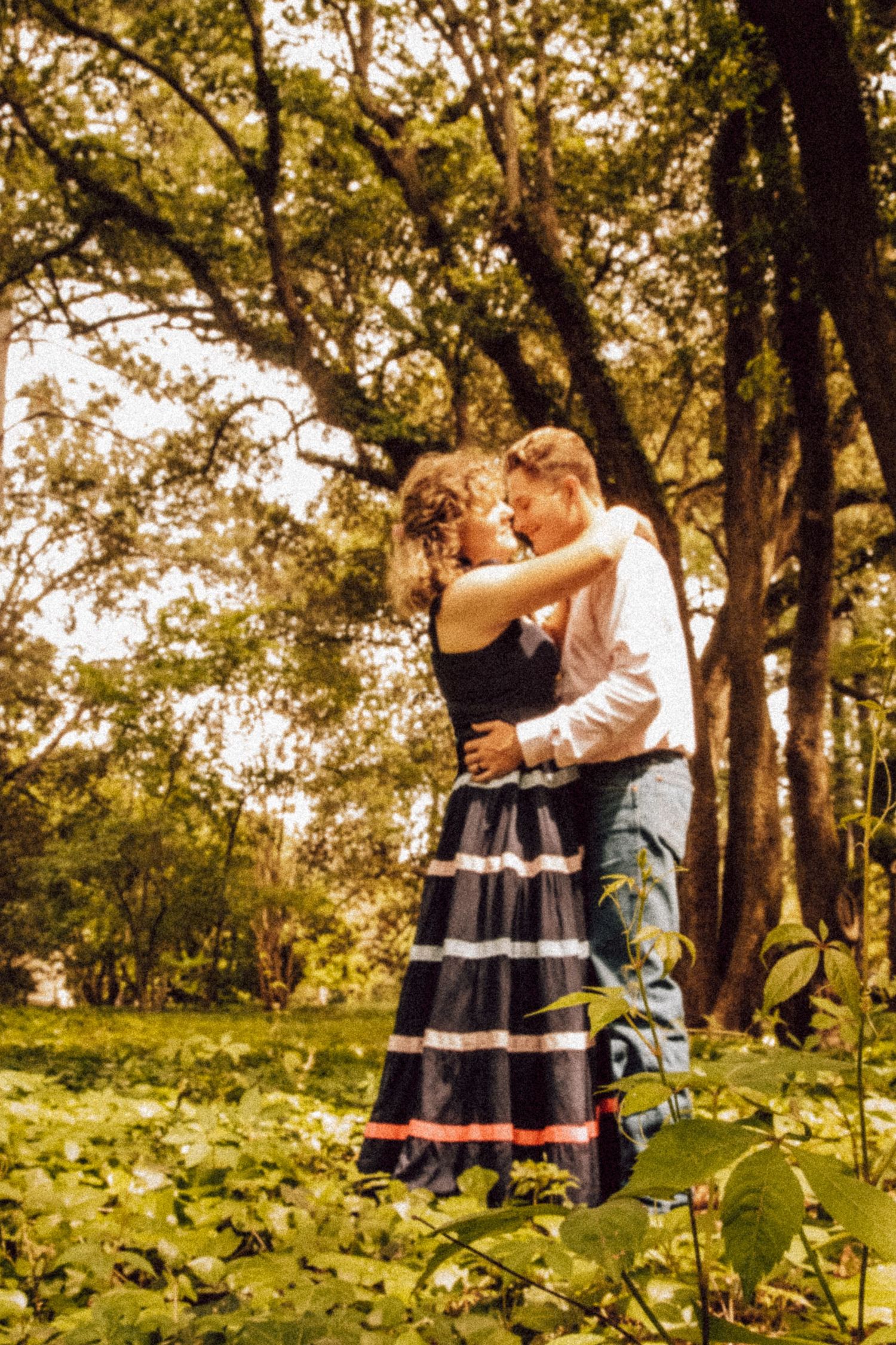 Romantic couple embracing in a sunlit garden with trees in the background.