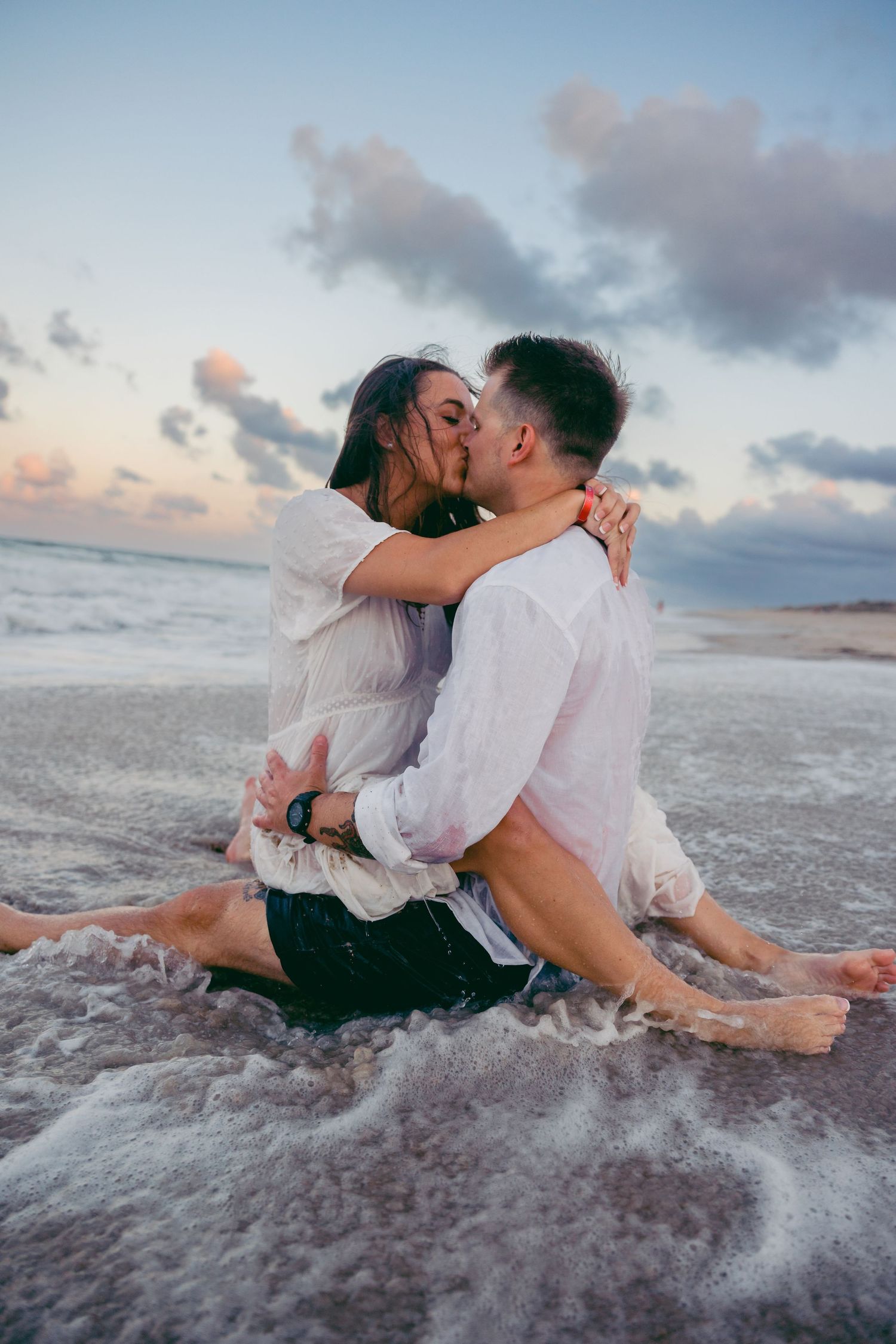 Romantic couple embracing in the ocean waves at sunset on a sandy beach.