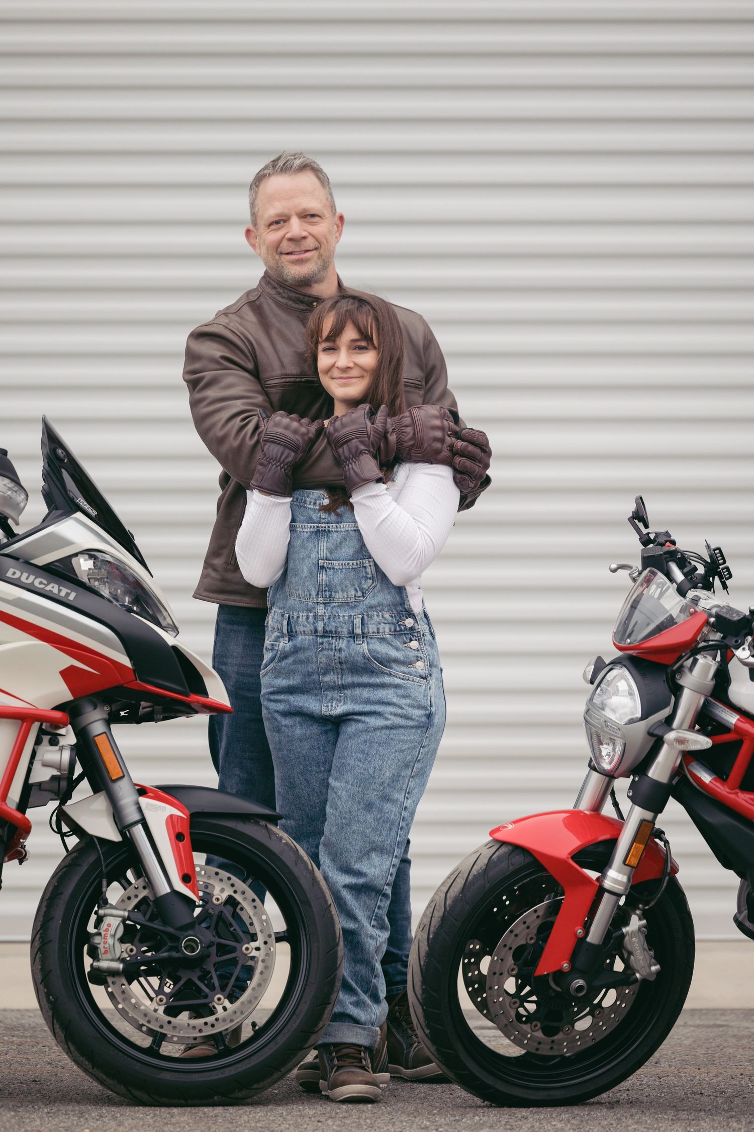 Couple posing with red and black motorcycles against white garage door background.