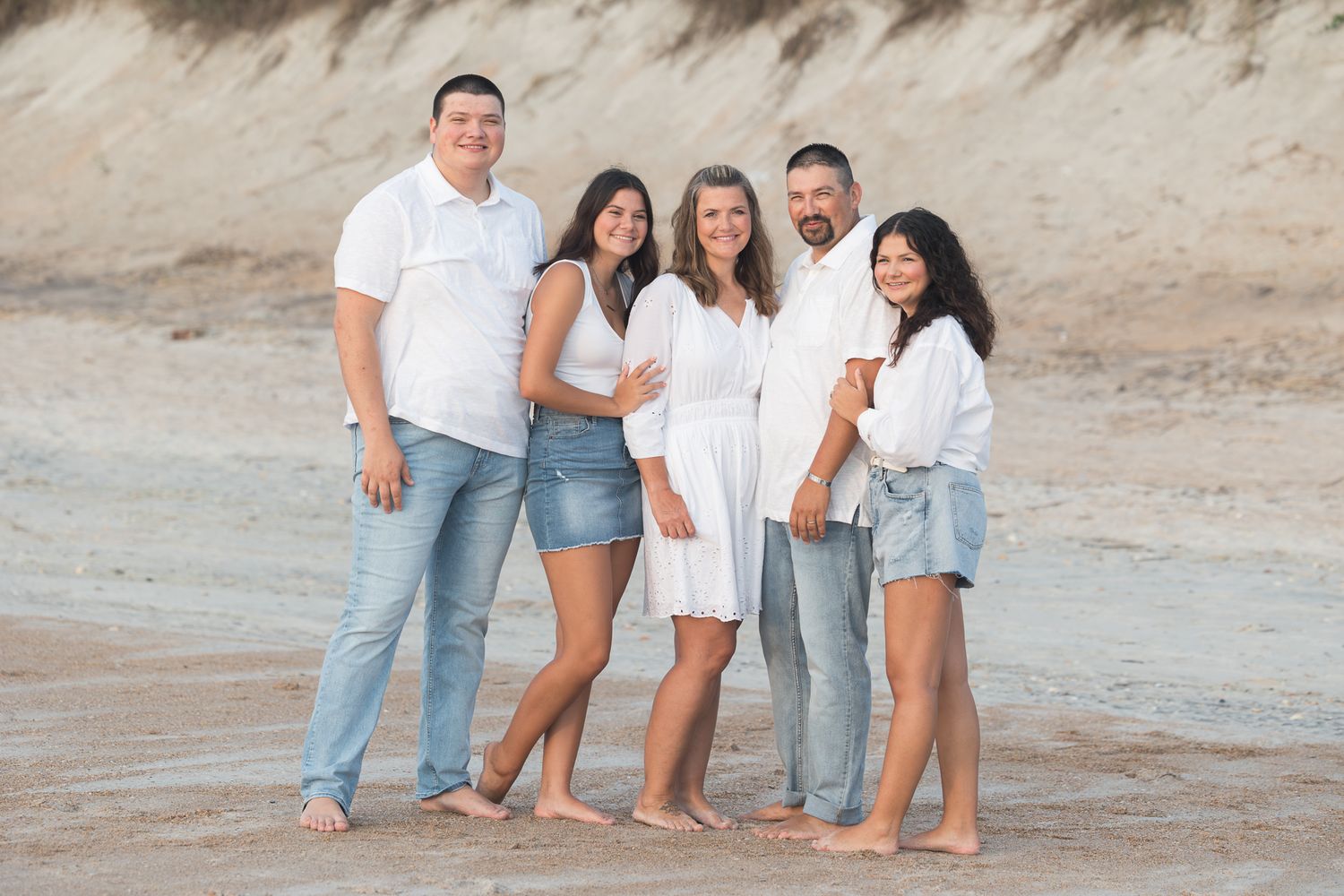 Family group wearing coordinated white and denim outfits on beach at sunset.