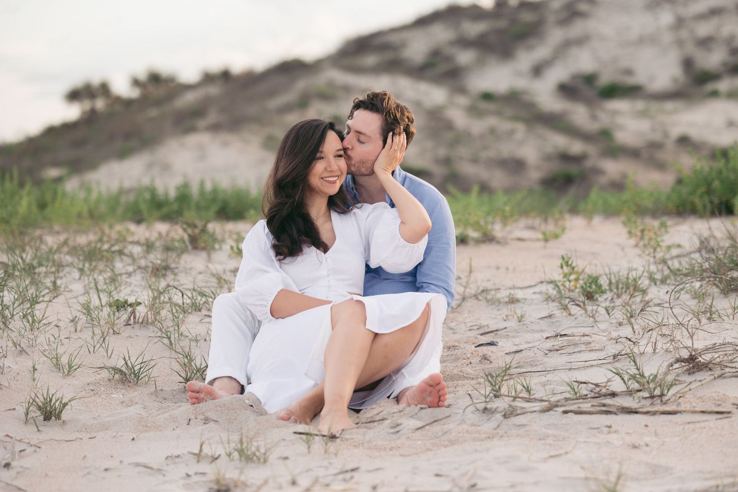 Family photoshoot on sandy dunes with white outfits at golden hour.