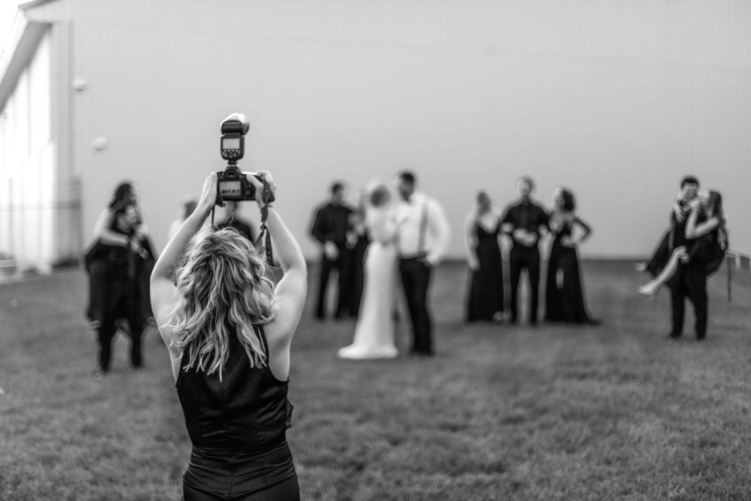 Professional photographer captures a wedding ceremony from behind while holding camera up high in black and white.