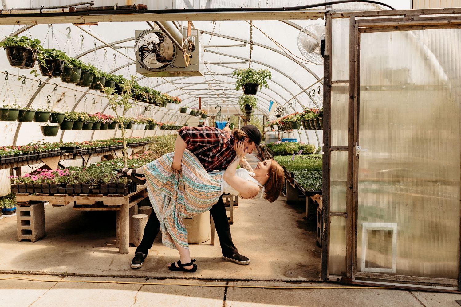 Couple together beside plants and seedlings in a large commercial greenhouse with multiple growing benches and aisles.