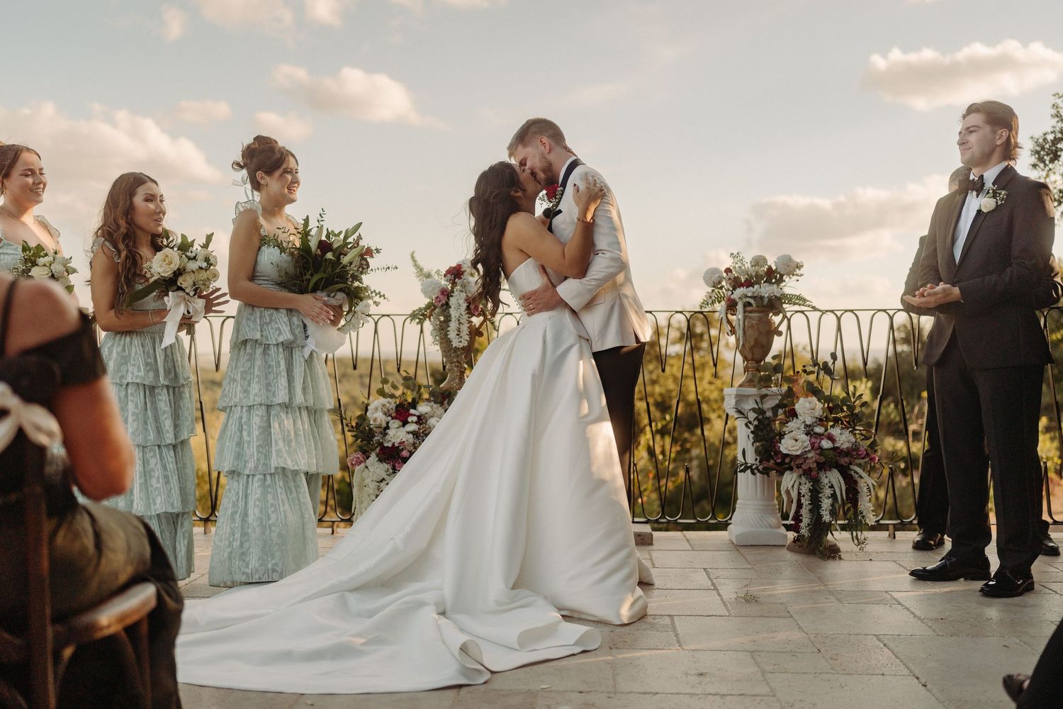 A couple shares their first kiss as newlyweds during an outdoor rooftop wedding ceremony at sunset.