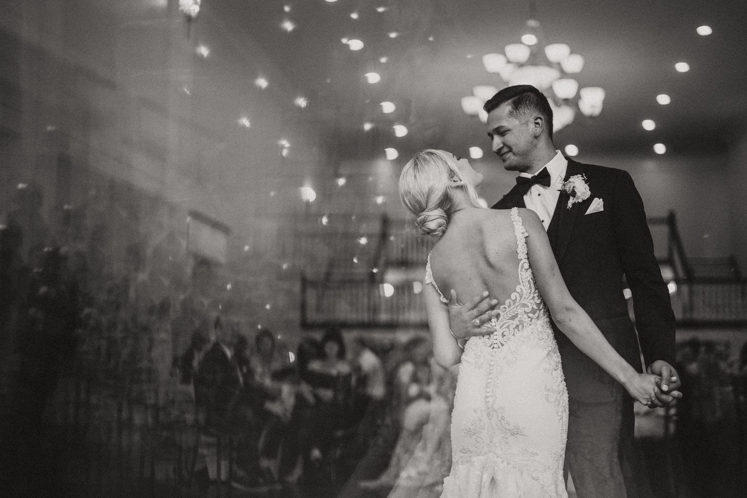 Black and white photo of a couple sharing their first dance at their wedding reception with twinkling lights overhead.