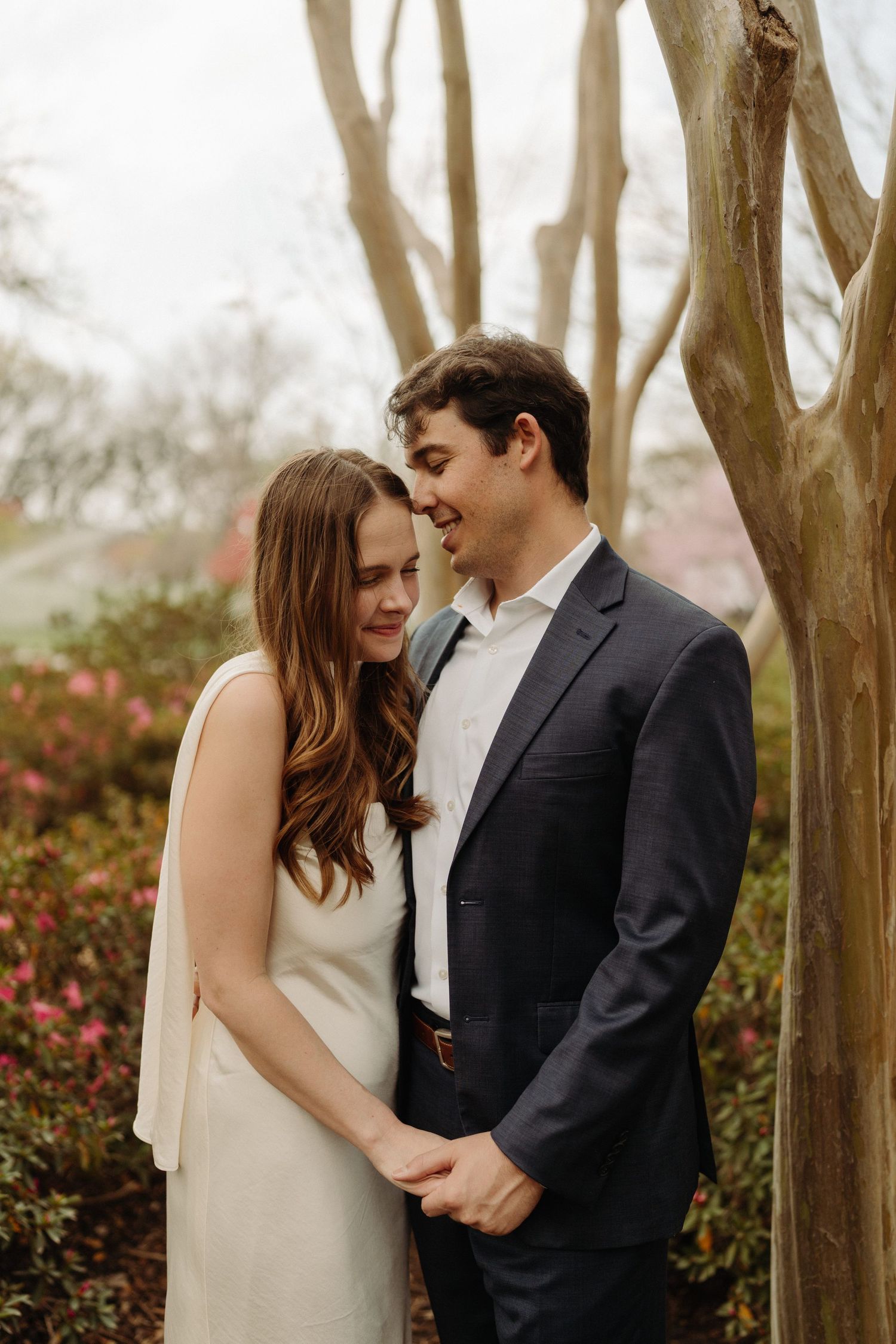 A romantic couple share an intimate moment among blooming trees on a misty spring day.