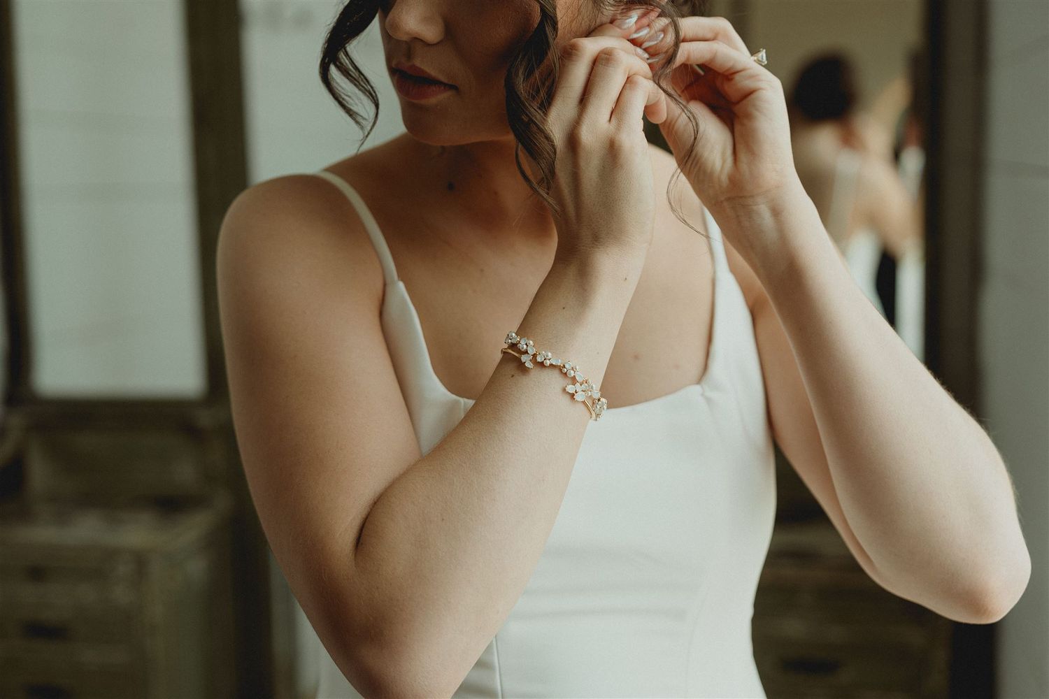 Close-up shot of someone in a white dress adjusting jewelry in soft natural lighting.