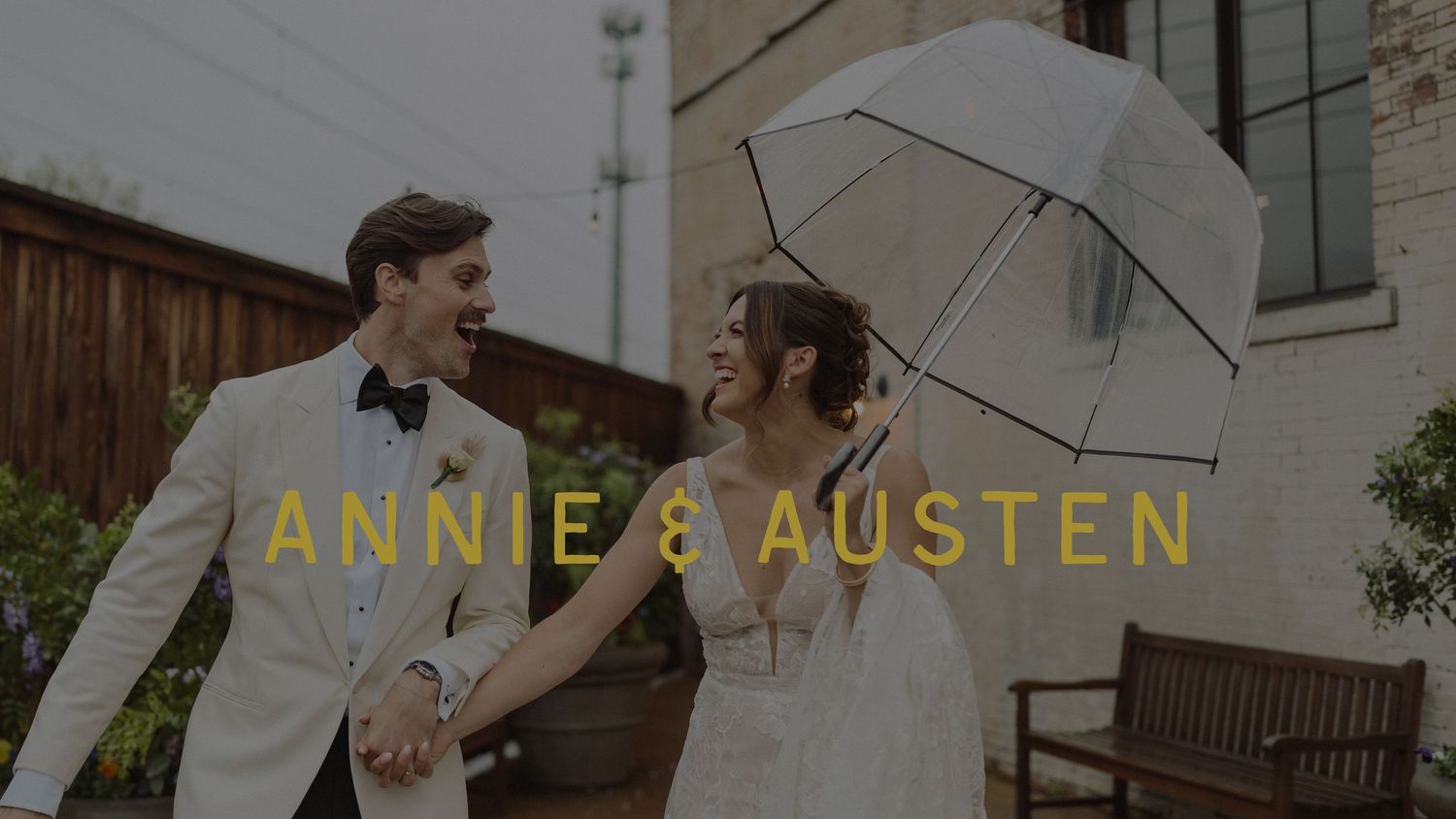 A bride and groom hold hands and smile under a clear umbrella on their rainy wedding day, with text reading Annie and Austen.