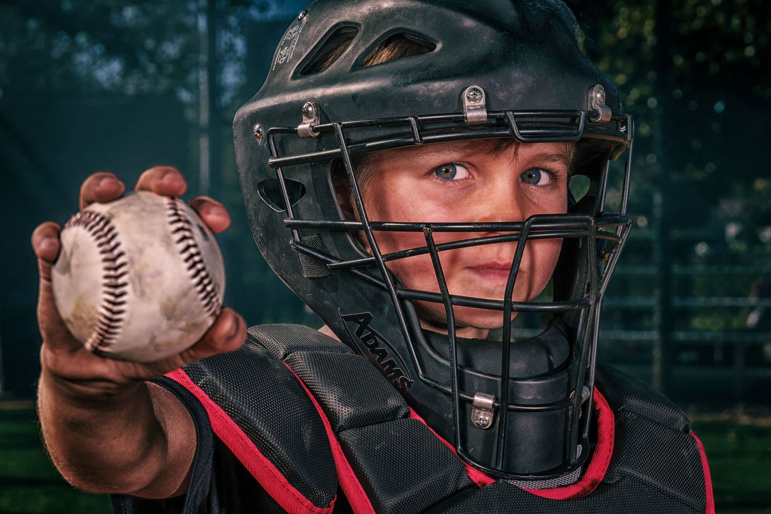 Close-up of baseball catcher holding ball while wearing protective mask and gear.