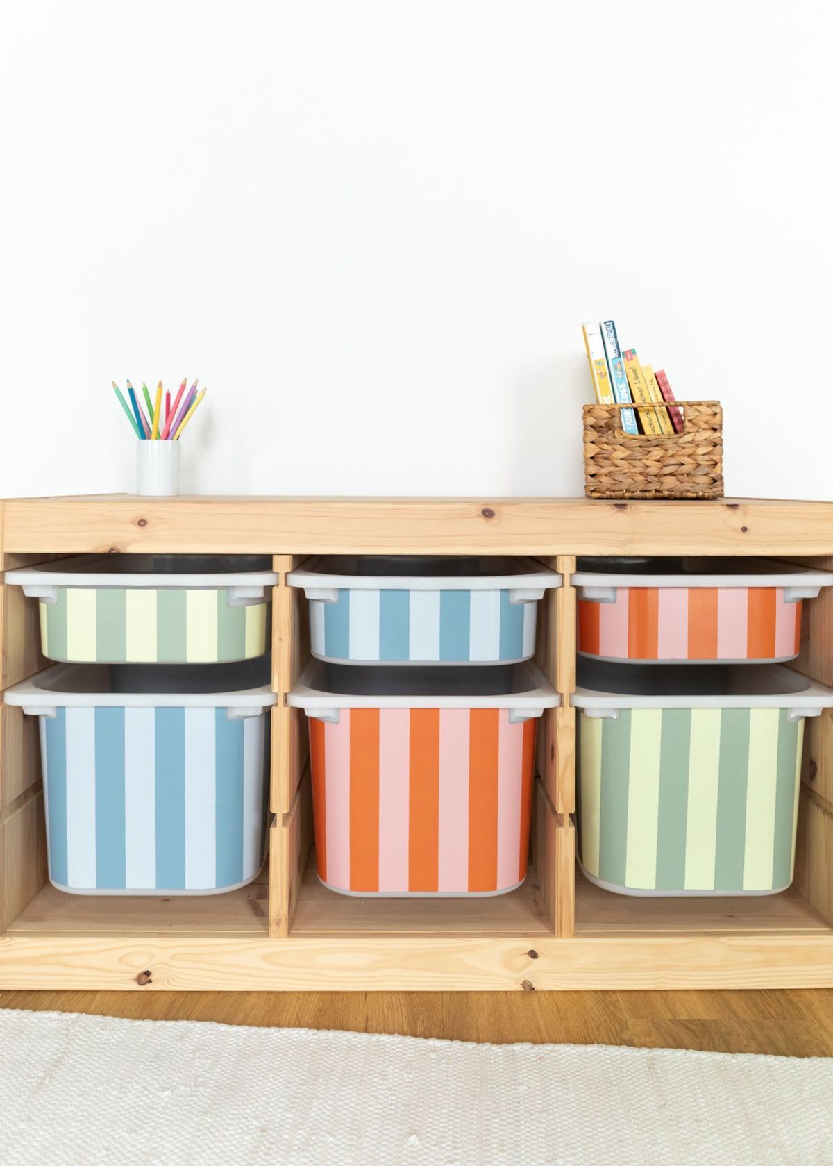 Colorful striped storage bins arranged neatly on wooden wall-mounted shelves for organized classroom or playroom storage.