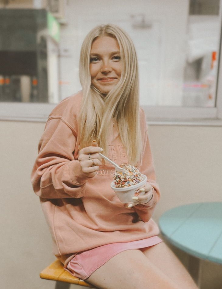 Person in pink sweatshirt lounging on turquoise couch while holding coffee cup in casual indoor setting.