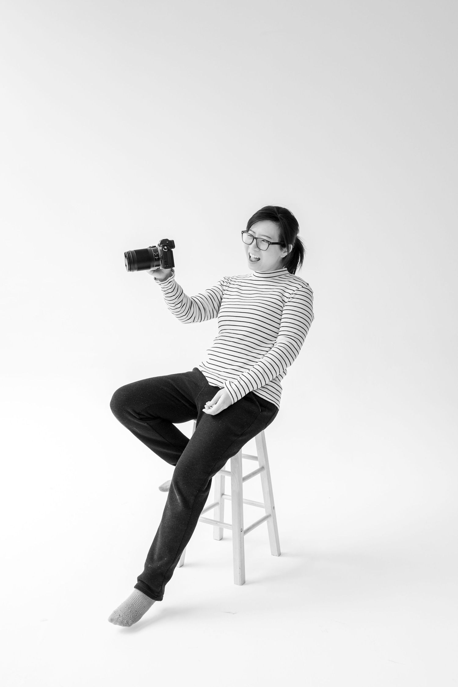 Person in striped shirt and dark pants sits on white chair in dynamic shooting poses against white background.