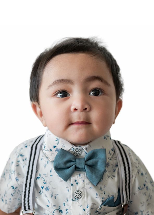 Adorable baby boy wearing a blue bow tie, suspenders, and floral shirt, posing for a portrait photo.