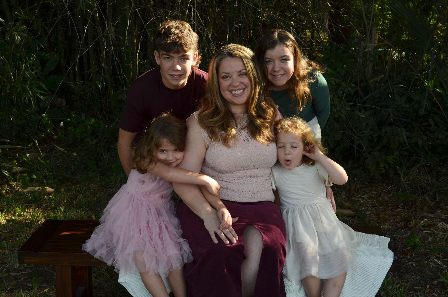 Family portrait of a smiling mother and four children posing together outdoors.
