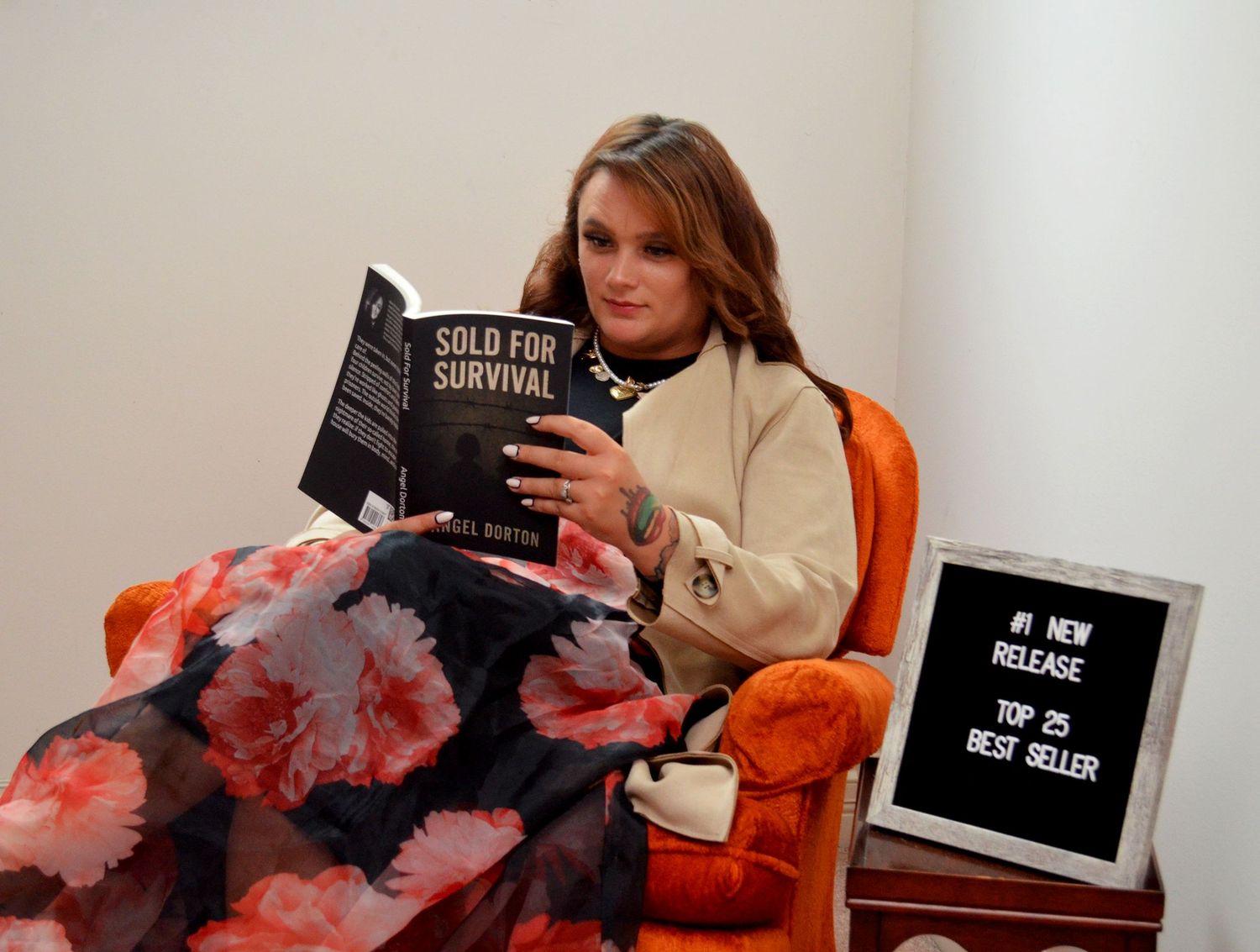 Woman in an orange armchair reads Sold for Survival beside a sign noting its new-release and bestseller rankings.