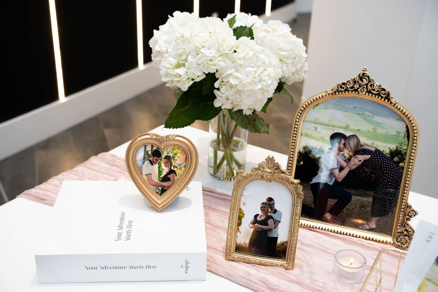 Engagement party table with framed couple photos, a white hydrangea bouquet, a guest book, and a small candle.