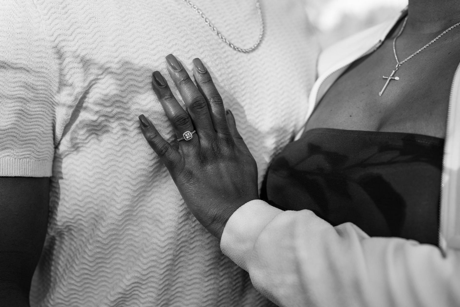 Black and white close-up of a woman's ringed hand placed on her fiancé's chest during an engagement shoot.