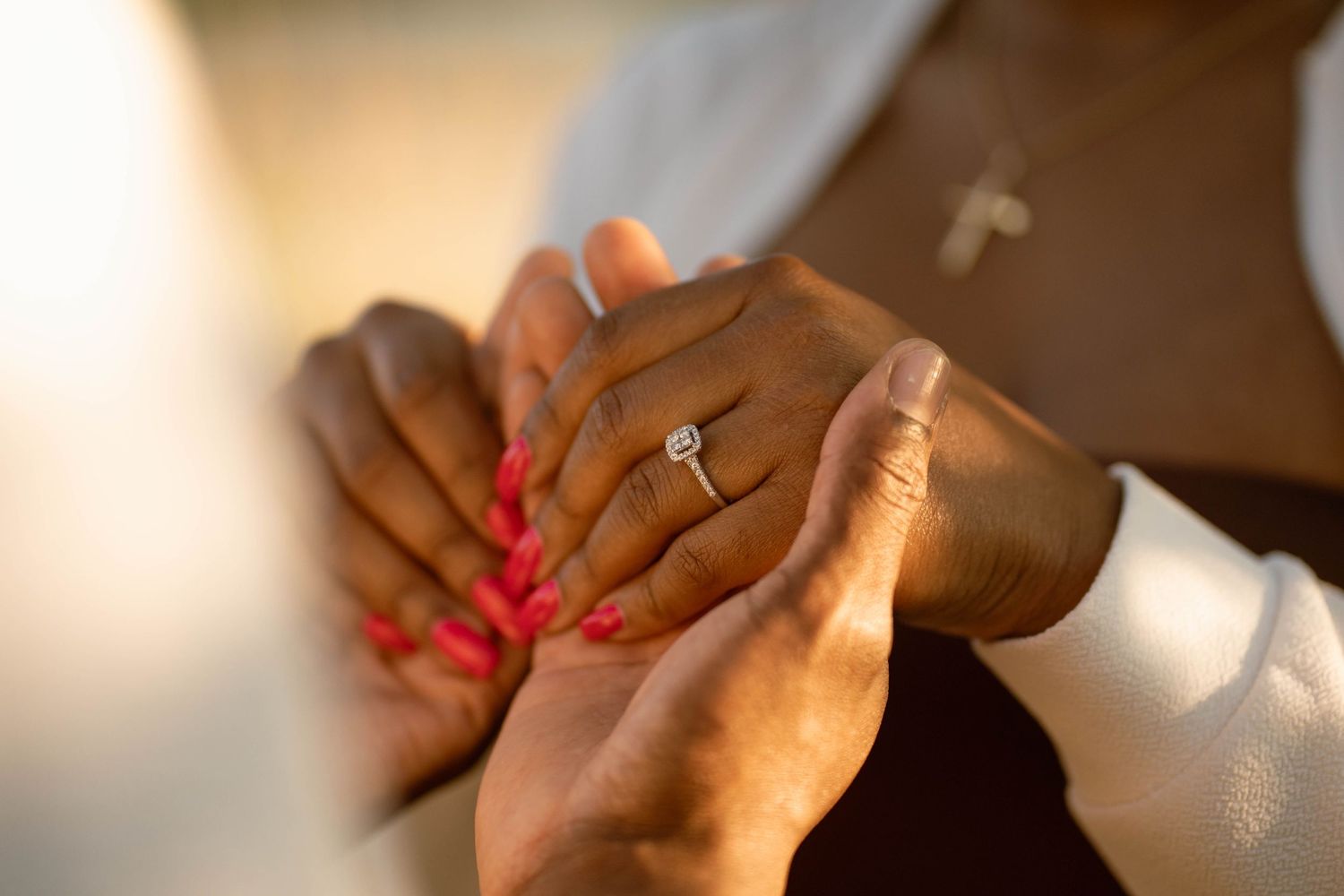 Close-up of a man holding a woman's hand with red nails, showing a sparkling diamond engagement ring.