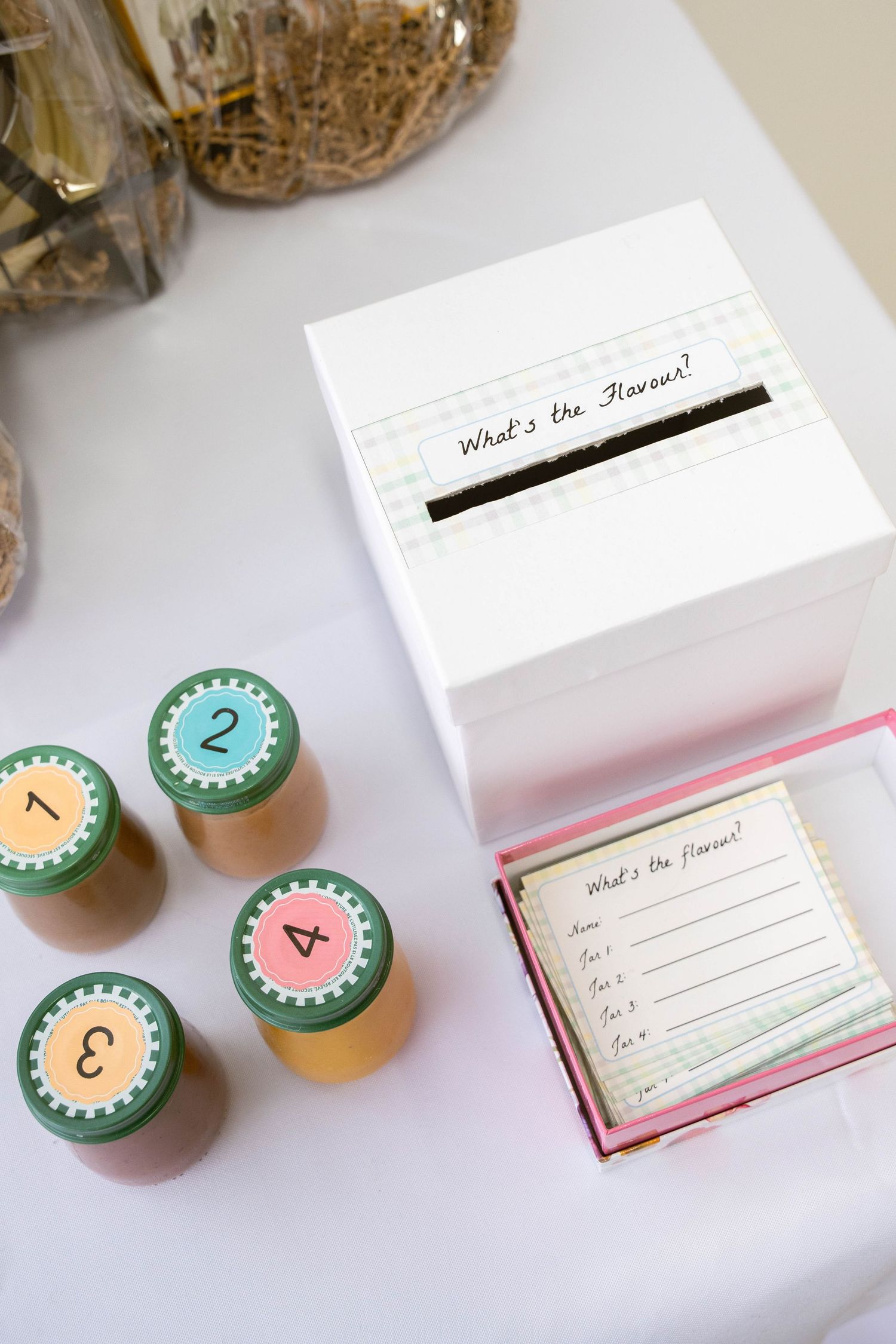 Baby shower guessing game with four numbered baby food jars, a white ballot box and cards titled What's the flavour.