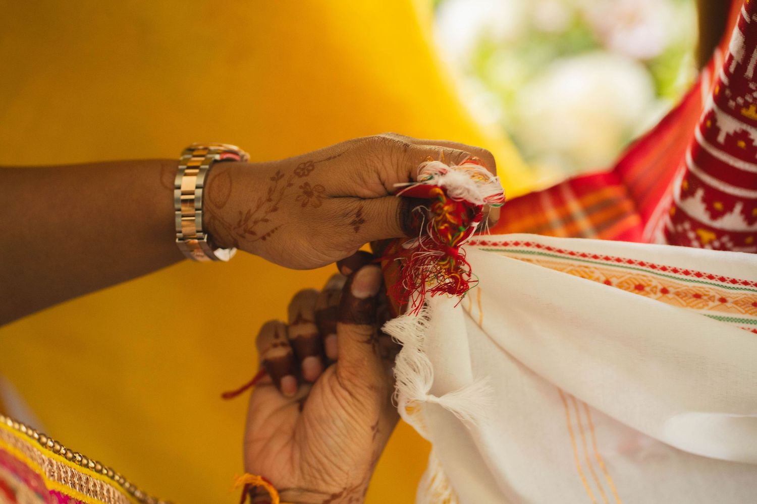 Close-up of a bride's henna-decorated hand clasping the groom's hand with a red cloth knot during a traditional Indian wedding ritual.