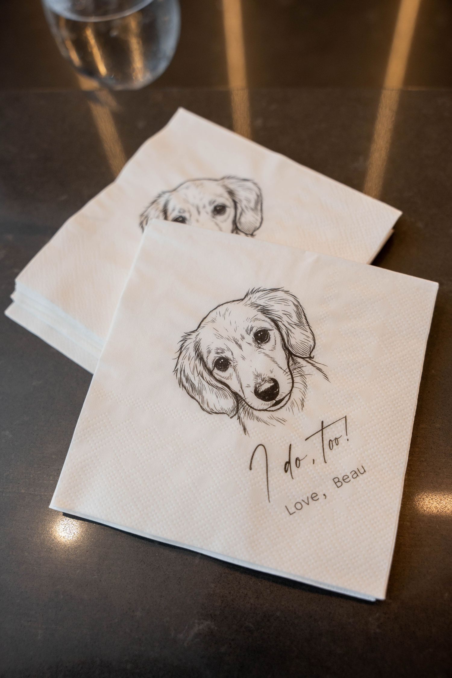 Stack of white cocktail napkins printed with a sketched dog portrait and the message I do, too! Love, Beau.
