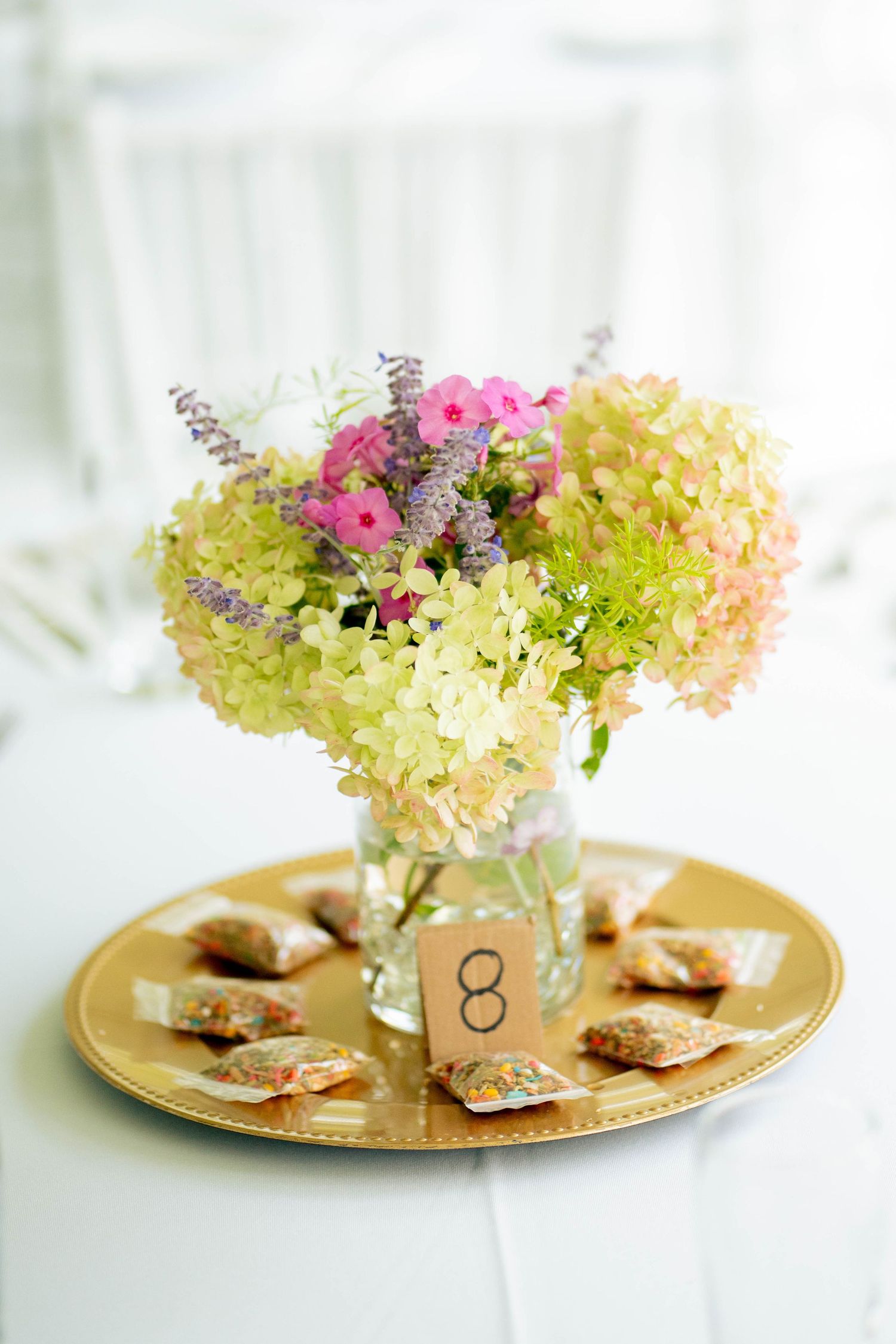 Wedding table centerpiece of pink and green hydrangea flowers in a glass vase with table number eight on a gold charger.