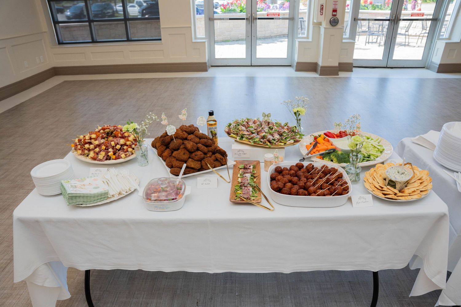 Baby shower buffet table with white linen, platters of appetizers, salads, and finger foods ready for guests.