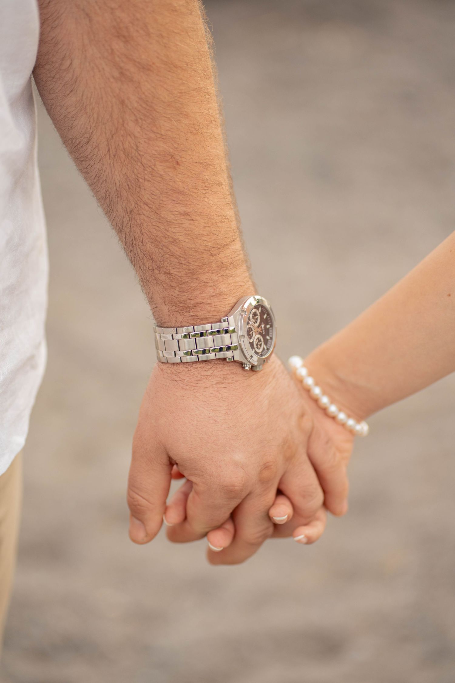 Close-up of a couple holding hands, the man wearing a silver wristwatch and the woman a pearl bracelet.