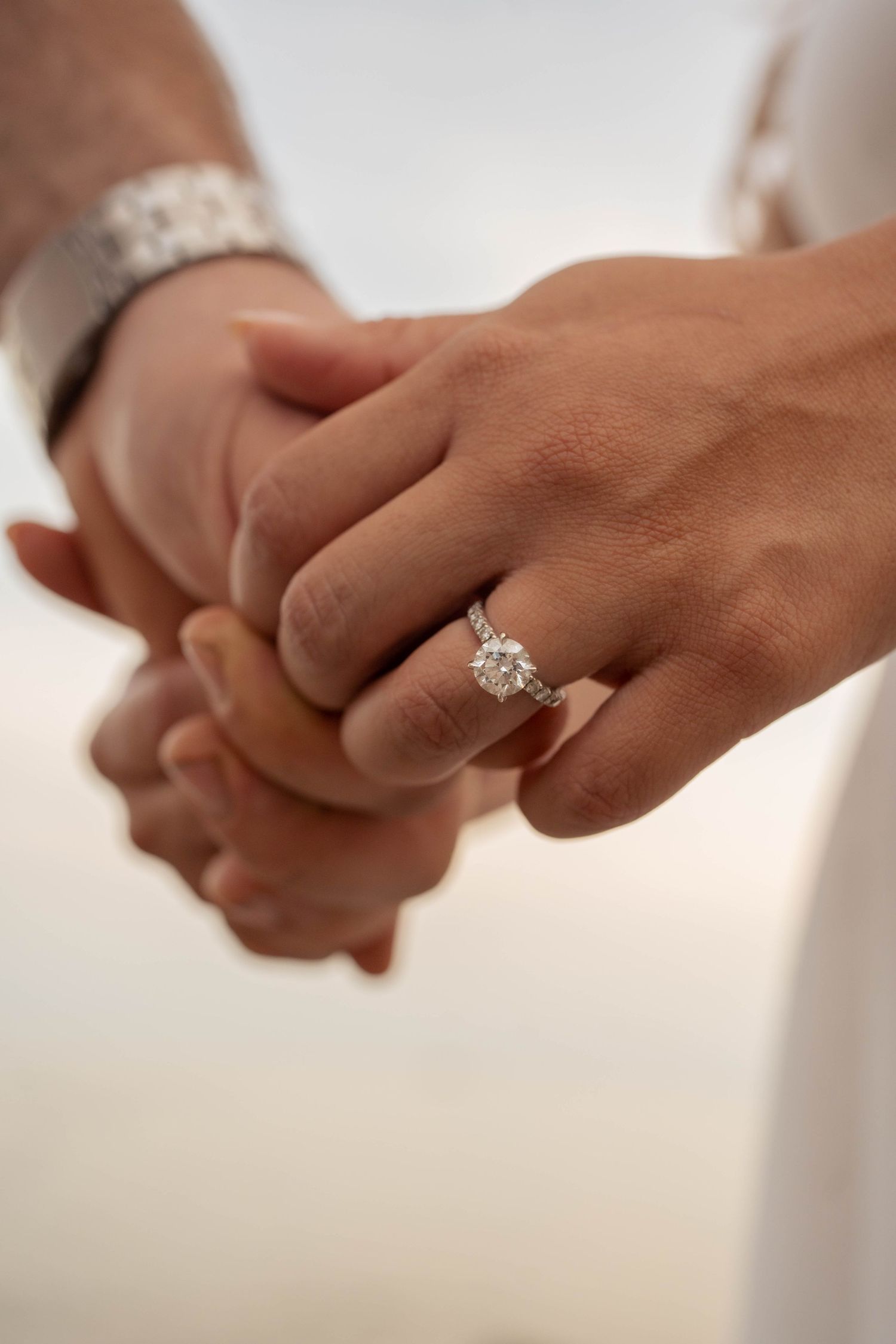 Close-up of a couple's clasped hands showing a sparkling diamond engagement ring on the woman's finger.