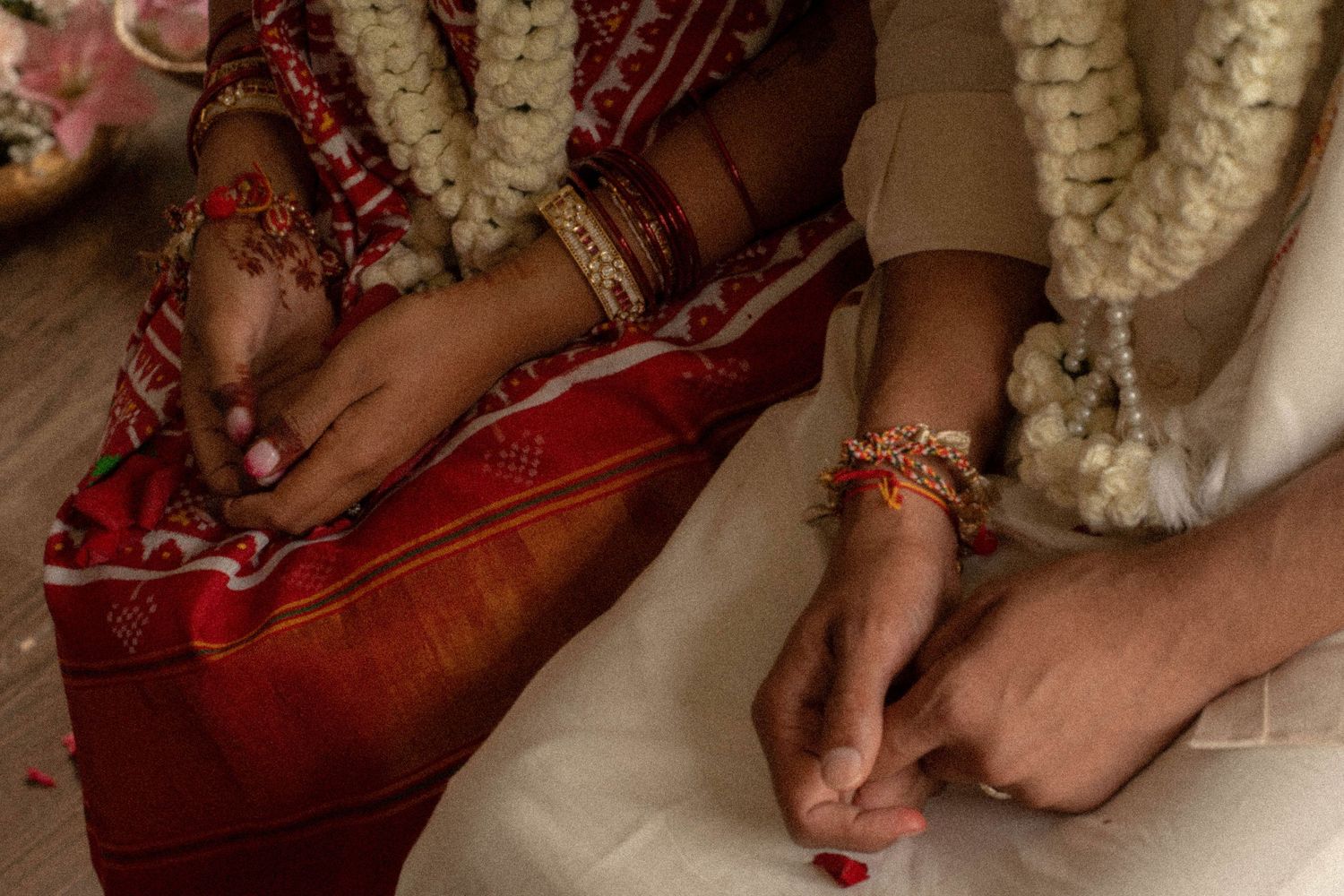 Close-up of a couple's hands adorned with red bangles, gold bracelets, and flower garlands during a traditional Indian wedding ritual.