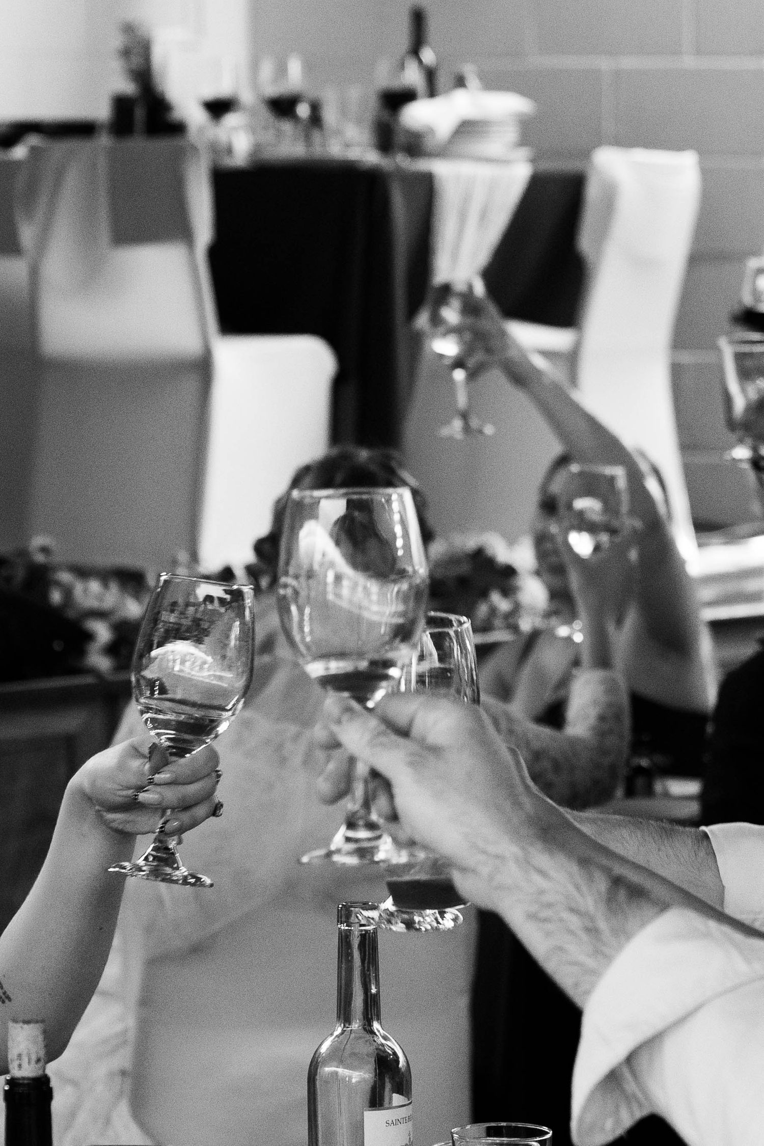 Black and white photo of guests raising wine glasses in a celebratory toast at a wedding reception table.