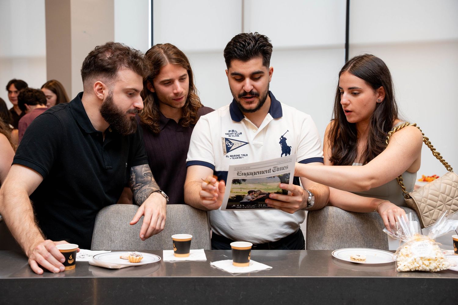Four friends sit at a table with espresso cups and pastries, reading a custom Engagement Times newspaper at a party.